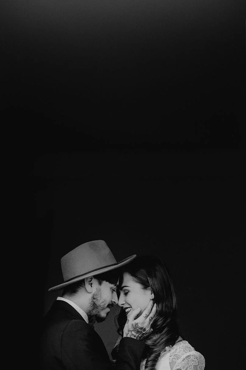 Ein Mann und eine Frau berühren sich liebevoll bei einem engen Blick. Der Mann trägt einen Hut und hat Tattoos an der Hand, die die Frau hält. Das Bild ist in Schwarz-Weiß gehalten.