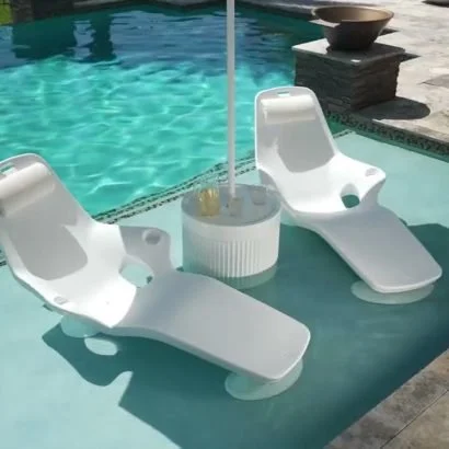 Two white pool lounge chairs partially submerged in a swimming pool, with a round side table between them and a pool umbrella pole.