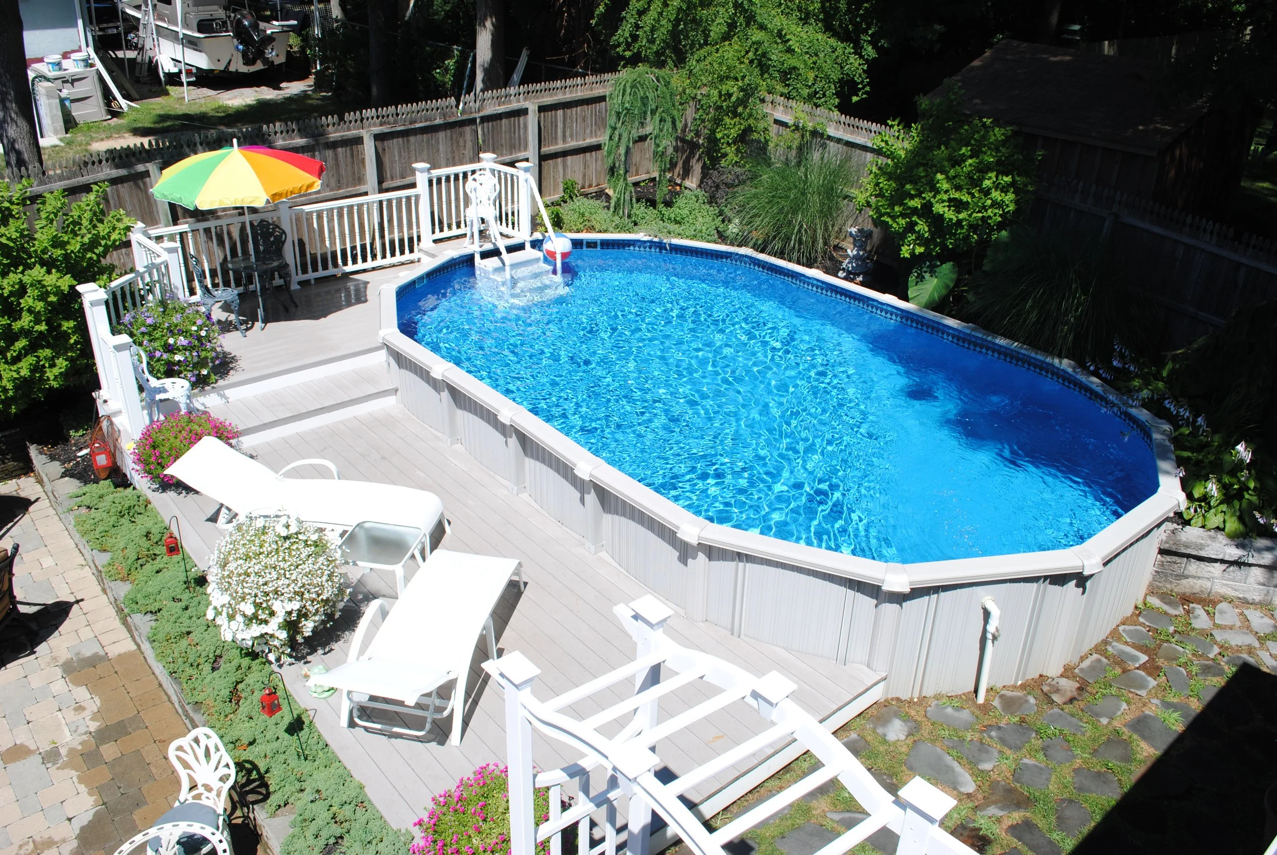 Backyard deck with a covered above-ground pool, surrounded by white fencing and a flower bed with various plants.