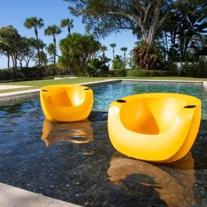 Yellow outdoor chairs in a pool with a tropical landscape and palm trees in the background.