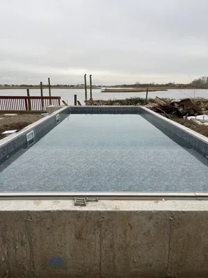 Empty swimming pool with water, overlooking a body of water and cloudy sky.