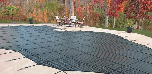 Pool cover on a backyard patio with chairs and trees in the background.