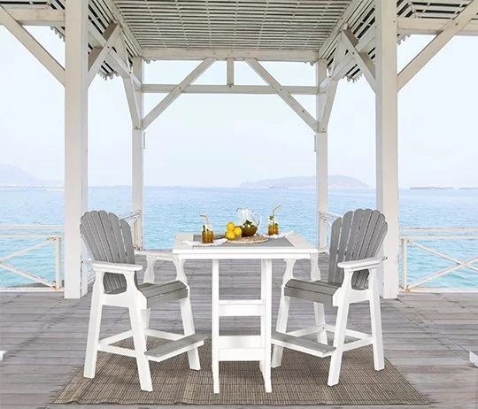 A white outdoor dining table with two chairs under a wooden pavilion overlooking the ocean, with a view of distant islands.