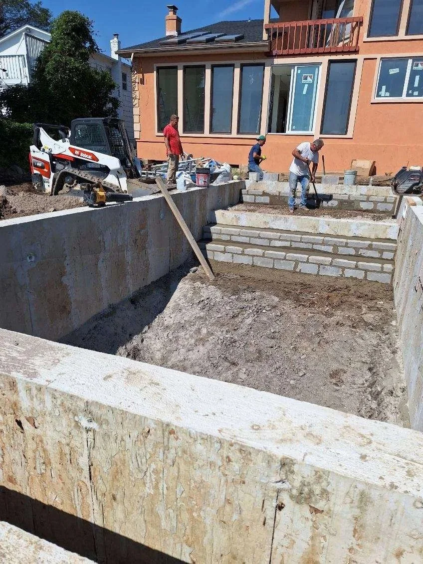 Construction workers building a staircase with bricks in the backyard of a house, with stairs leading up to the house's patio.