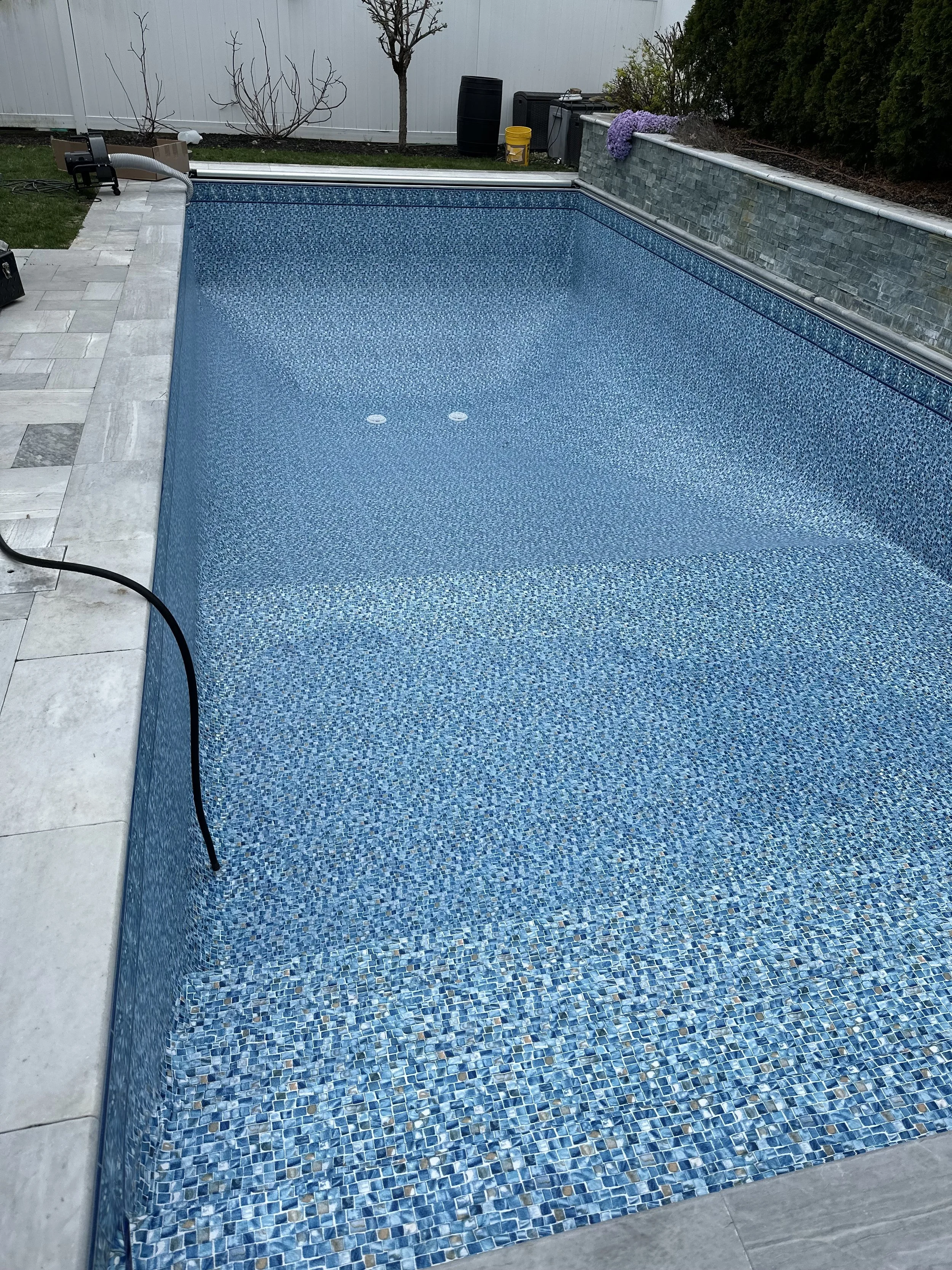 Modern house with hot tub on patio, surrounded by greenery and flowers, during daytime.