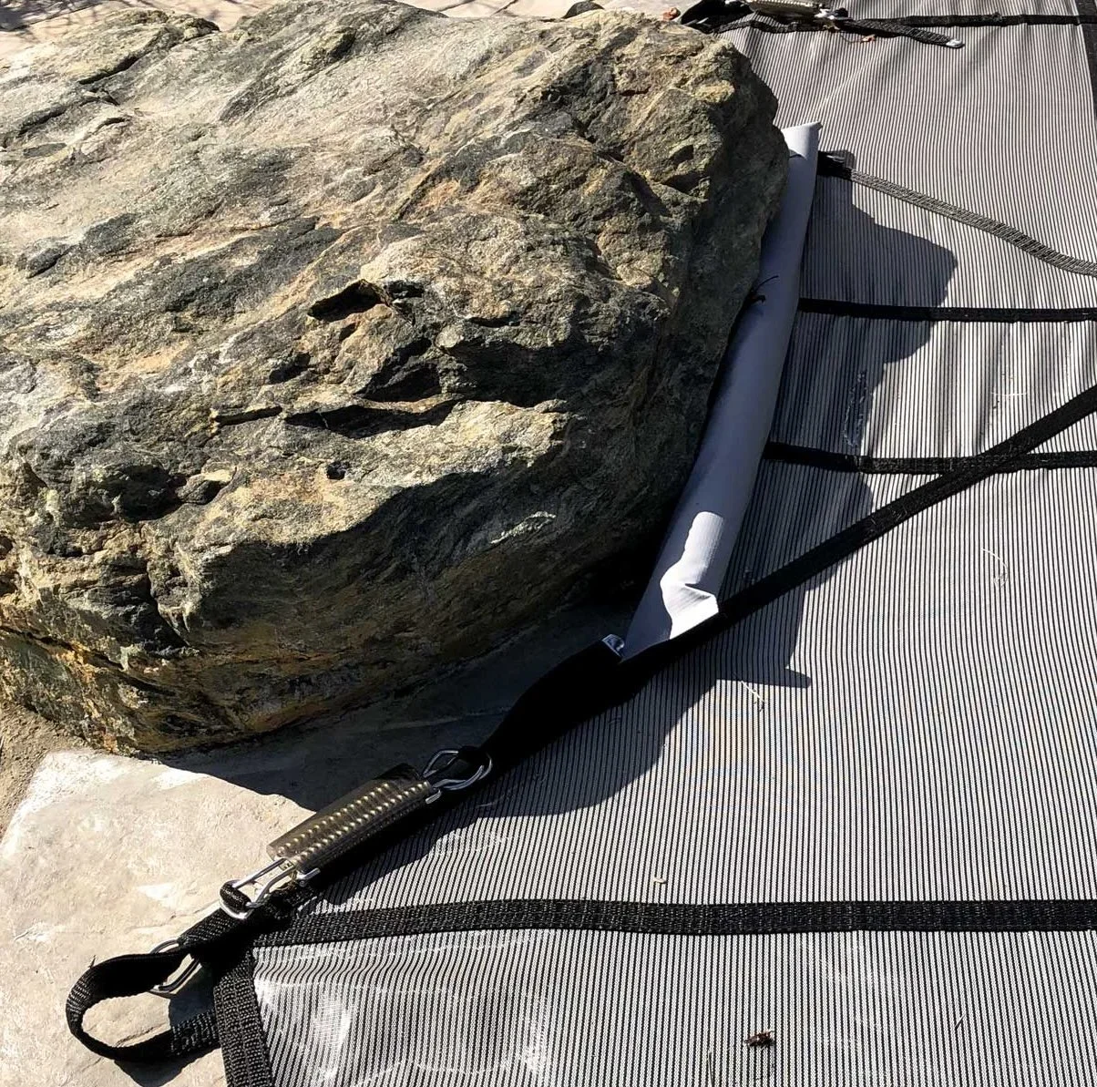 Close-up of a large rock on a textured outdoor mat with a roller and black straps, captured in bright sunlight.