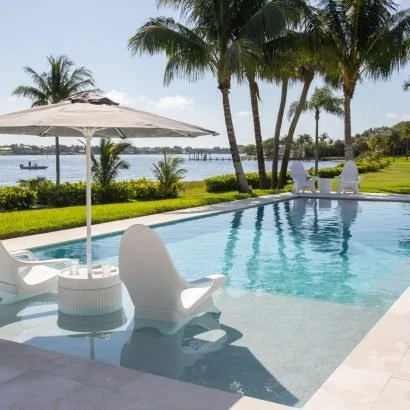 Luxurious swimming pool in tropical outdoor setting with palm trees and a view of a lake or river.