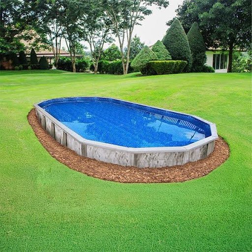 A small, oval-shaped backyard pool with blue water, surrounded by well-manicured green grass and landscaping, including neatly trimmed bushes and trees.