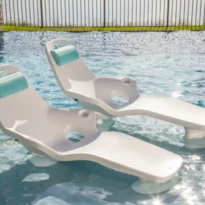 Two white plastic pool lounge chairs partially submerged in a swimming pool.