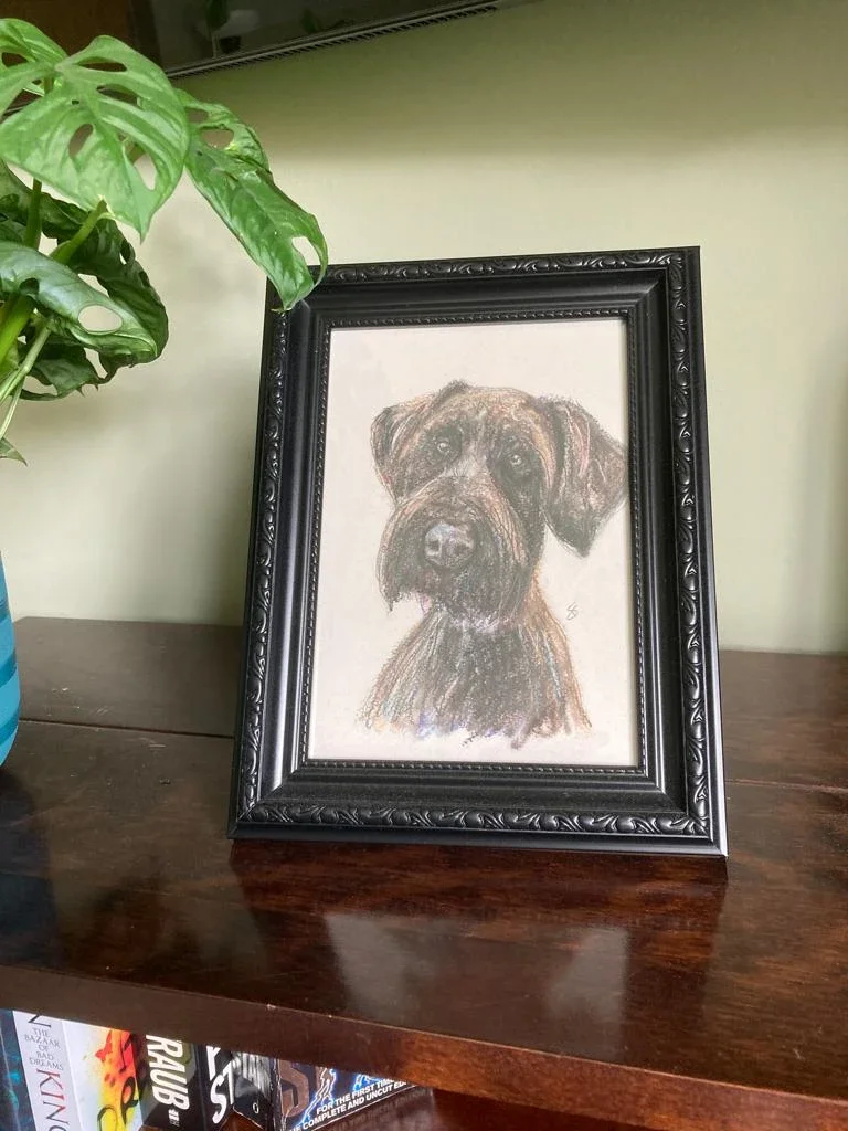 A framed Quick&Quirky portrait of a dog placed on a wooden surface next to a green plant.
