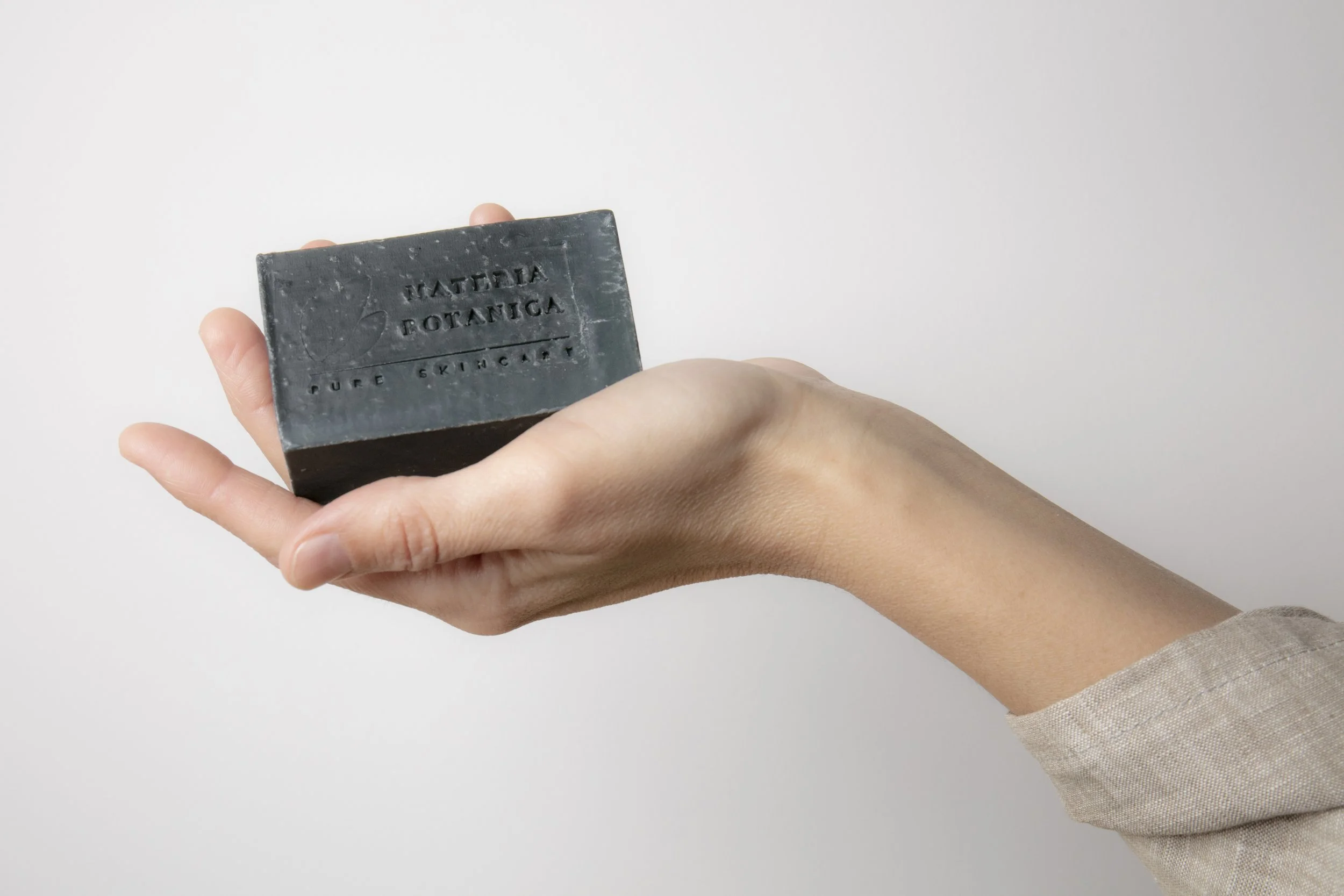 A hand holding a bar of black soap labeled 'Patricia Botanica Pure Skincare.'