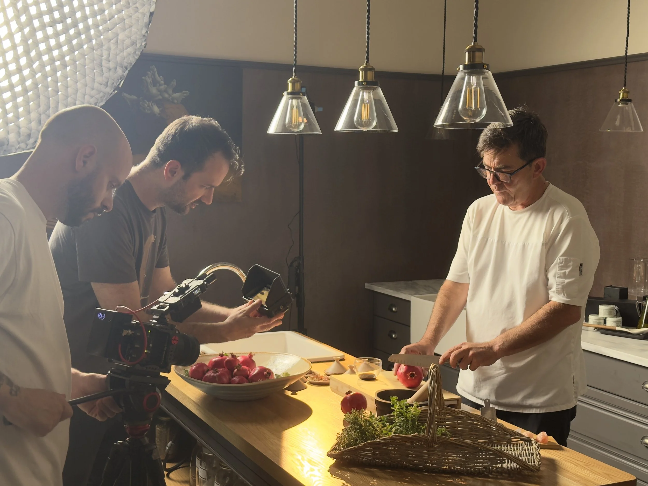A chef preparing food while filming crew captures the process with camera in a professional kitchen.