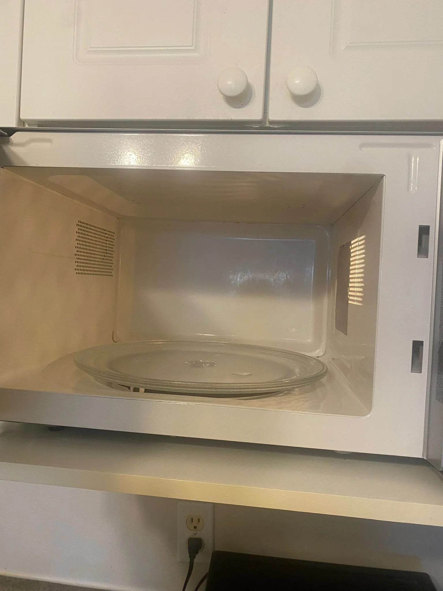 Empty microwave oven with a glass plate inside, white exterior, and some vents on the sides.