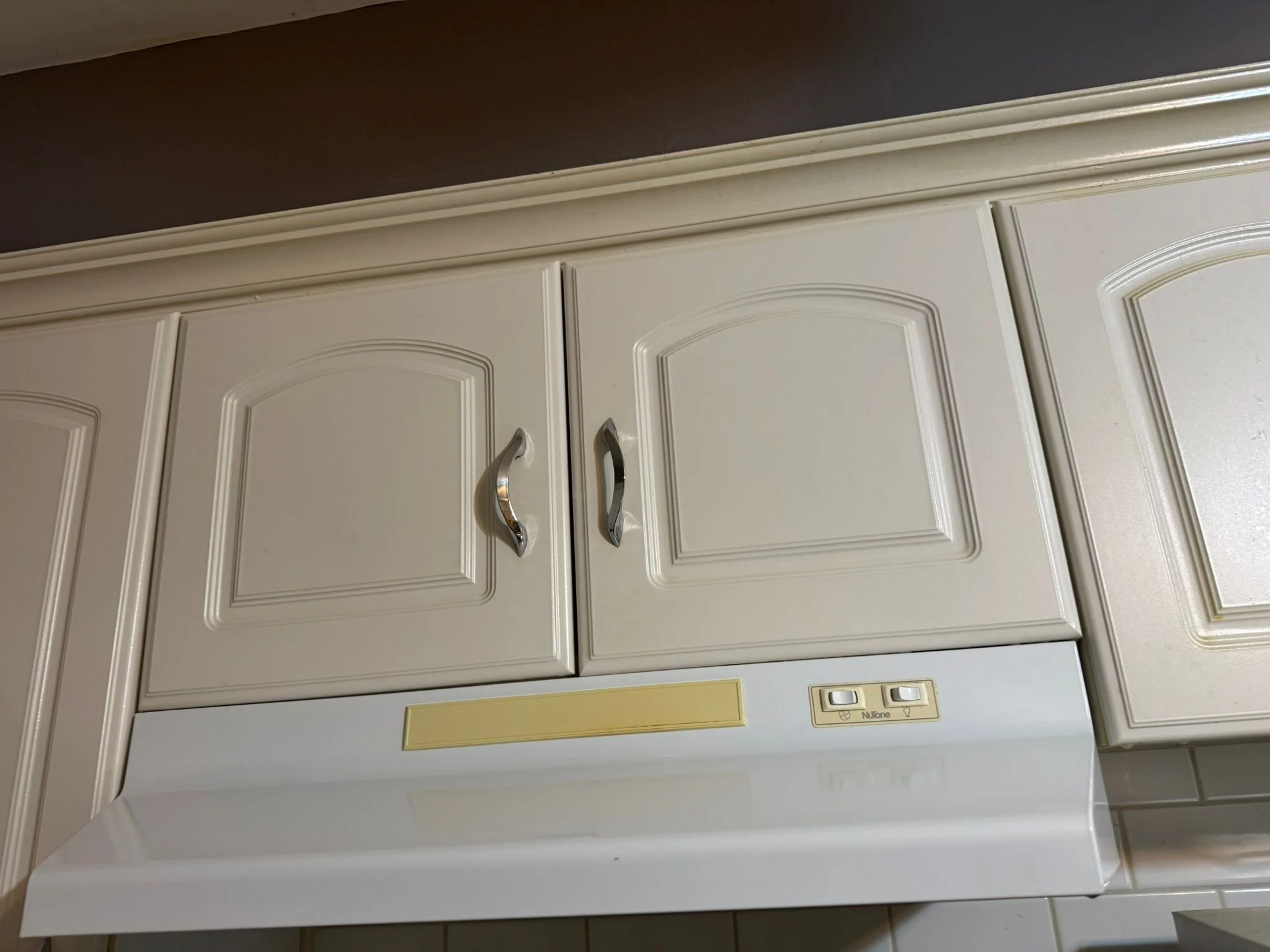 Kitchen cabinets with silver handles above a white stove with a beige control panel.