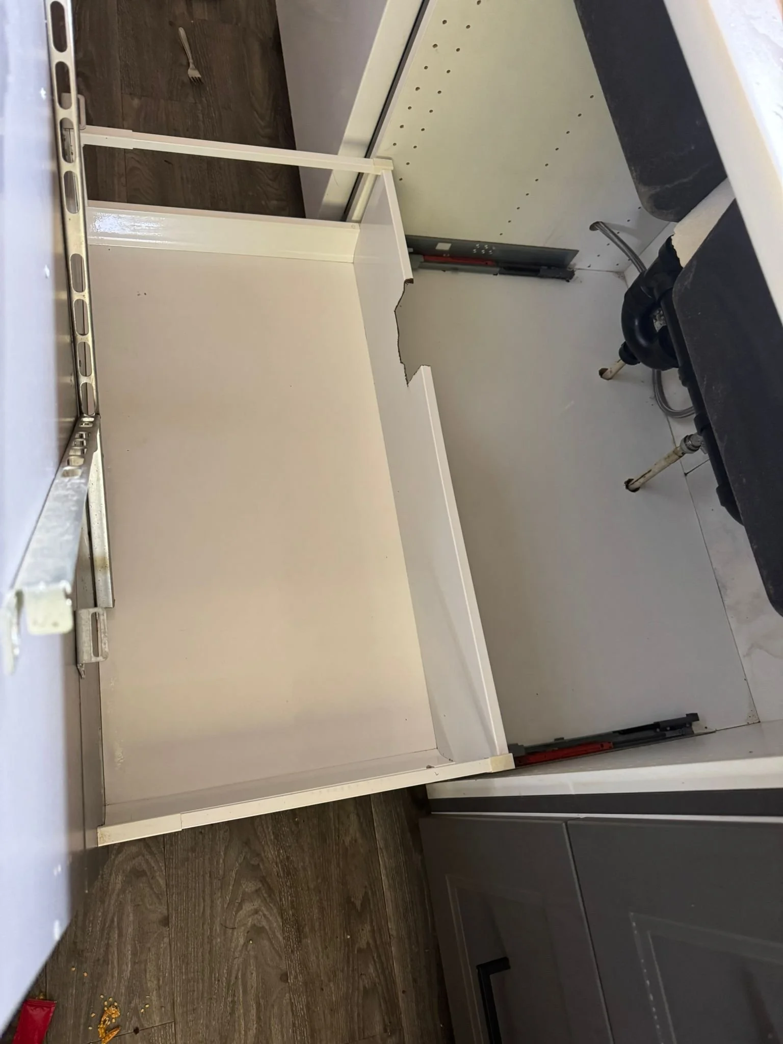 A partially assembled cabinet or shelving unit in a kitchen under construction, with visible metal frame and incomplete white panels, next to a gray cabinet and black countertop. Construction tools and materials are present.