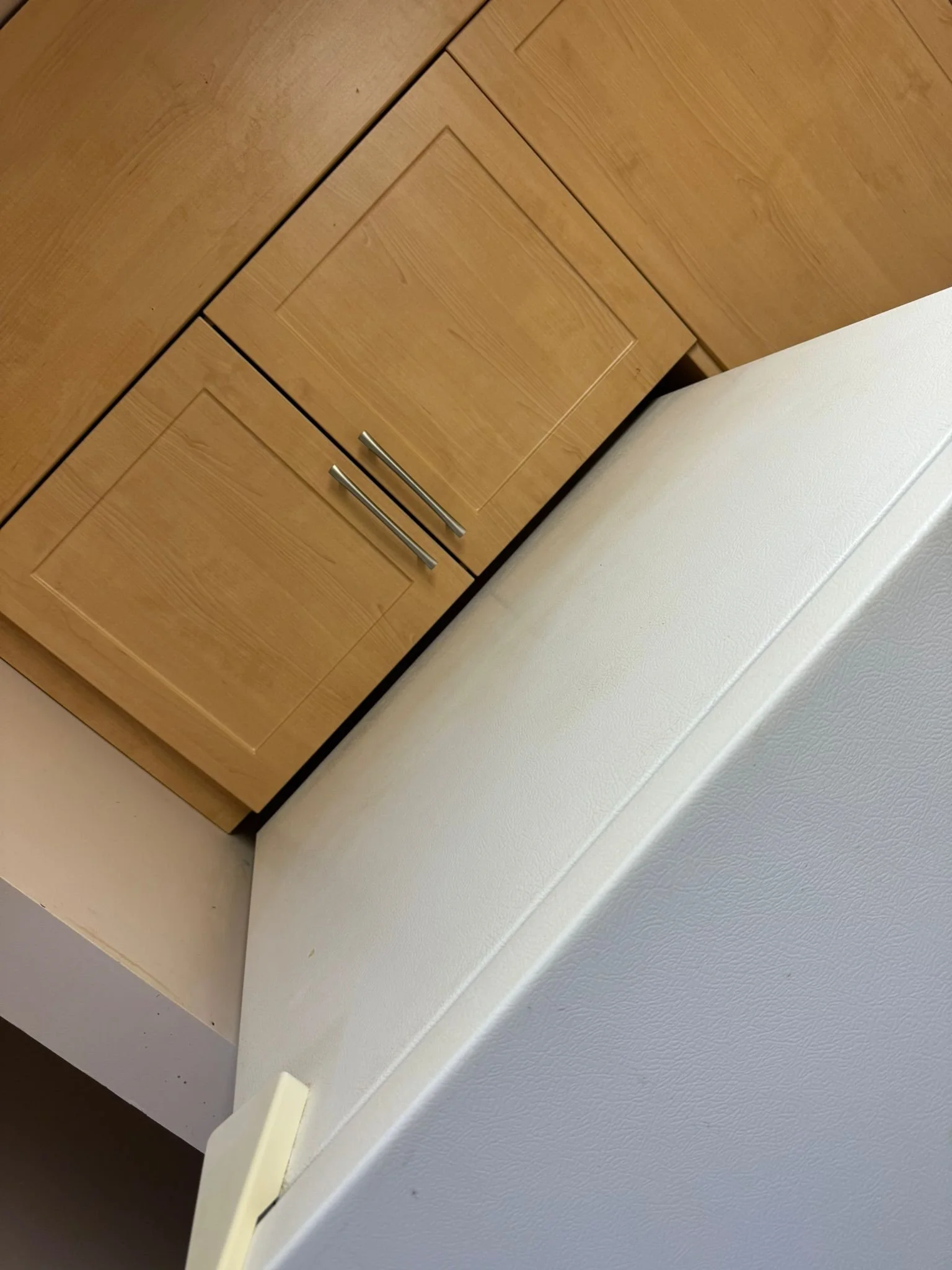 Close-up of a wooden cabinet with two drawers next to a white textured wall and a beige surface.