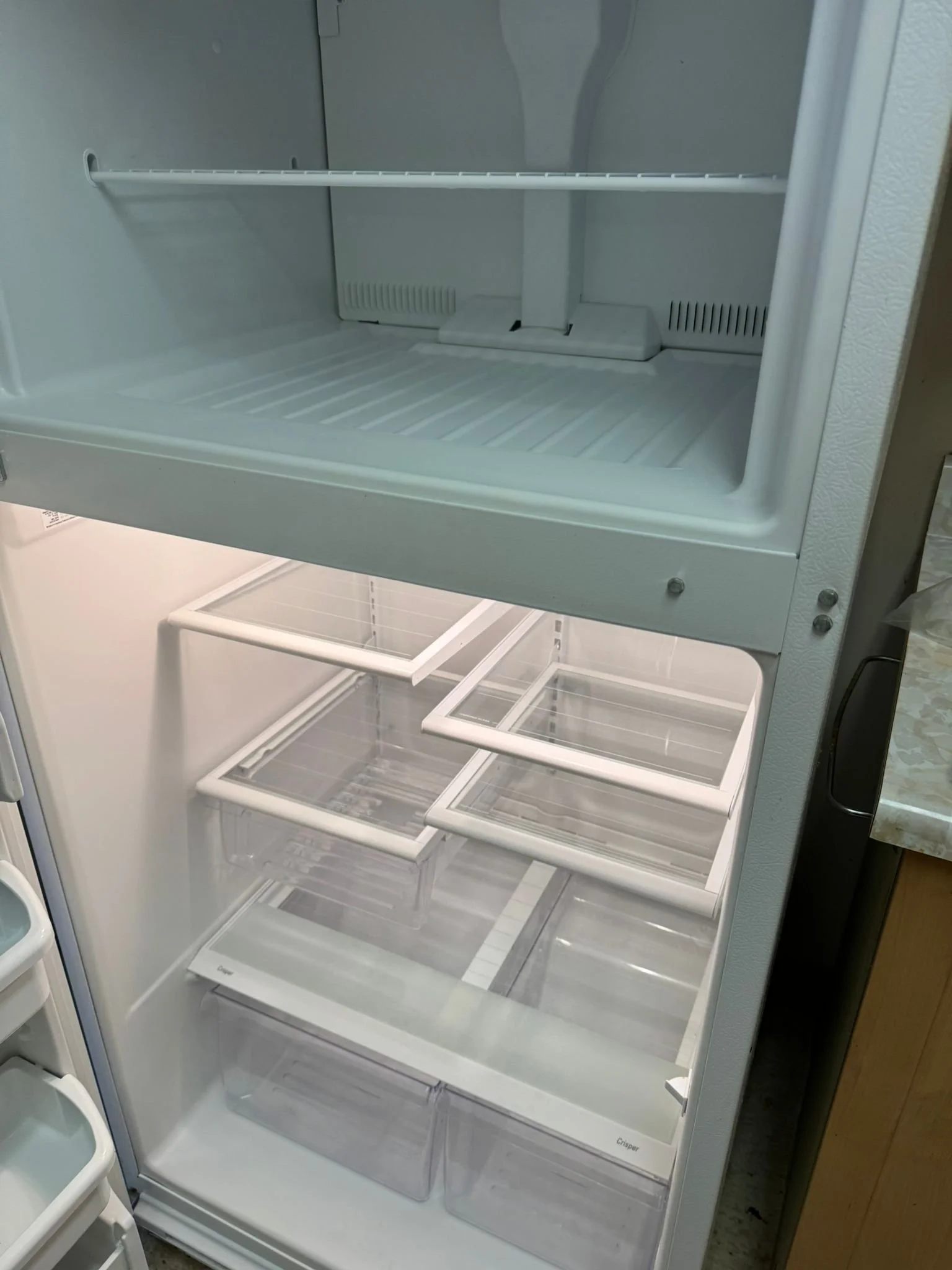 An empty refrigerator with two sections; the top section is the freezer with no items inside, and the bottom section is the refrigerator with several empty shelves and drawers.