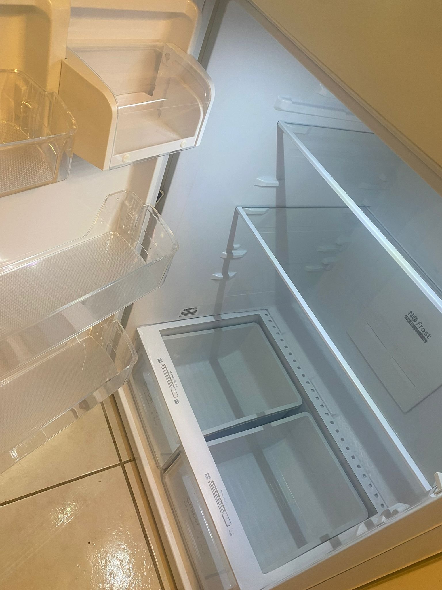 Empty refrigerator with open door, glass shelves, and clear plastic bins on a tiled floor.
