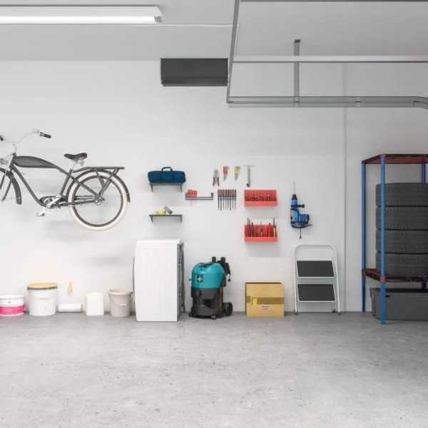 Garage with bicycle mounted on the white wall and various tools and supplies on shelves and the floor.