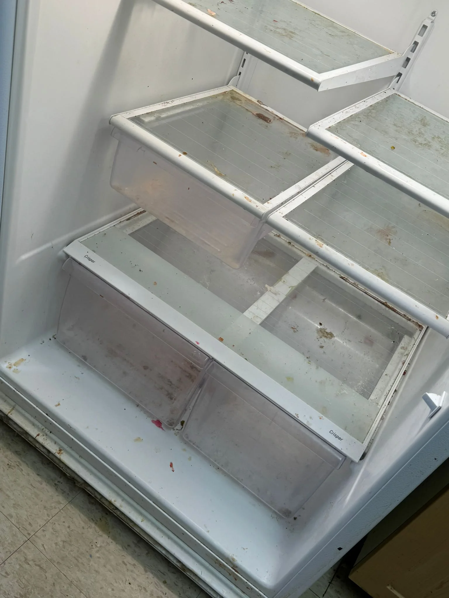 Empty, dirty, open refrigerator with multiple shelves and drawers.