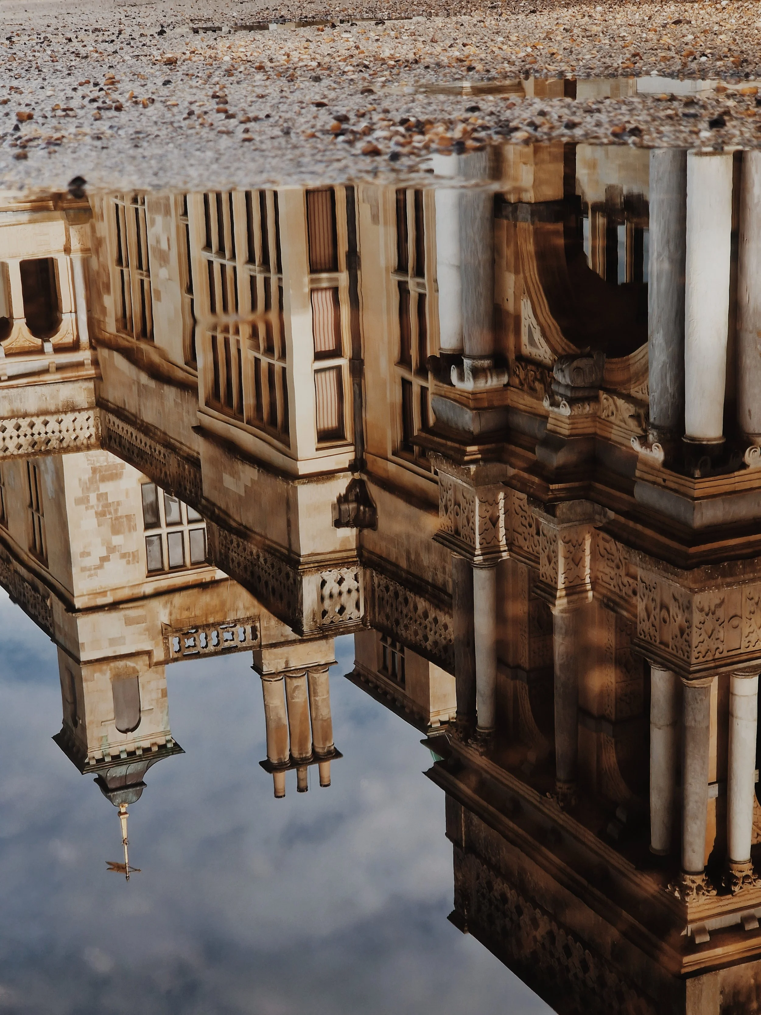 Reflection of a historic architectural building with columns, windows, and intricate stone details in a puddle of water.