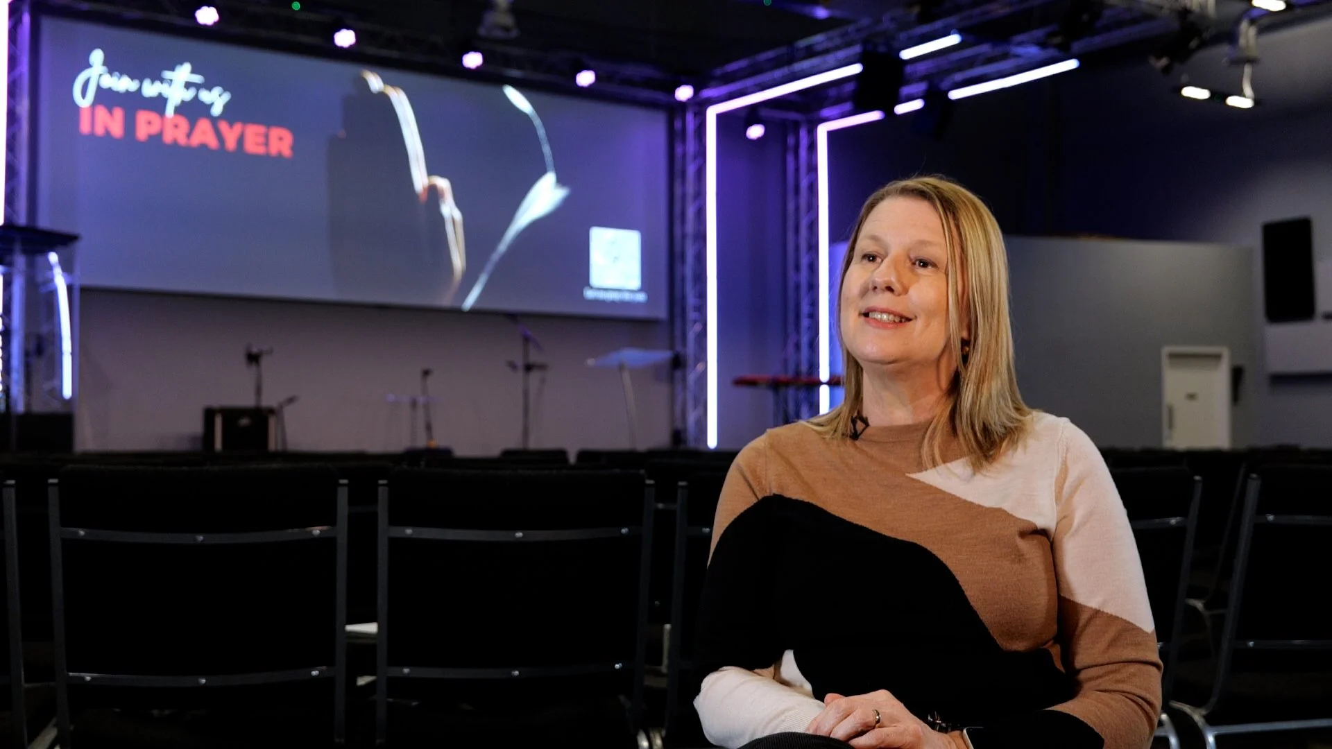 A woman sitting in a church, talking head style. Purple backdrop. Joe Beynon Media