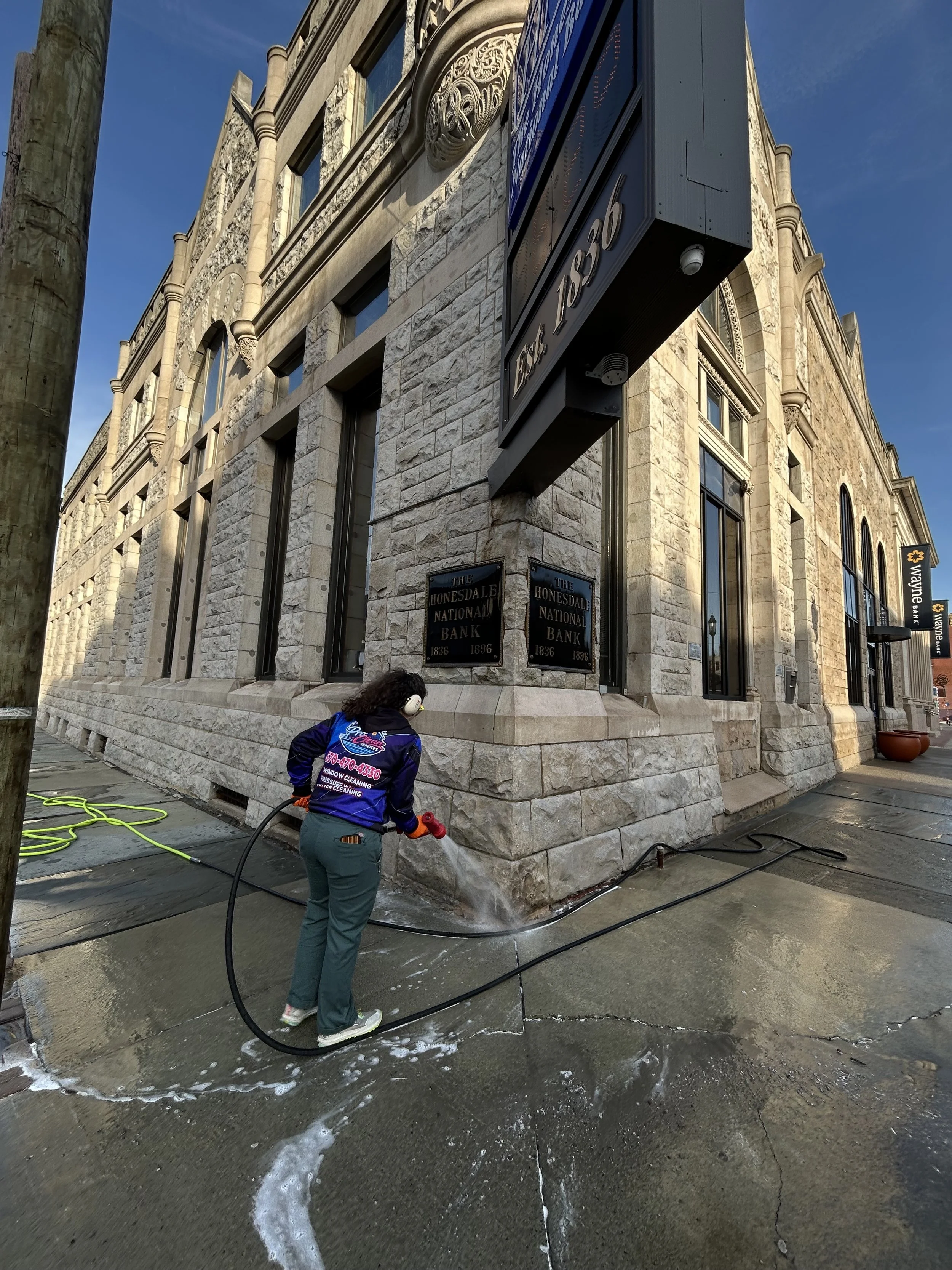 Pressure washing service cleaning a commercial sidewalk outside a stone building in NEPA by Pro Clean Services NEPA.
