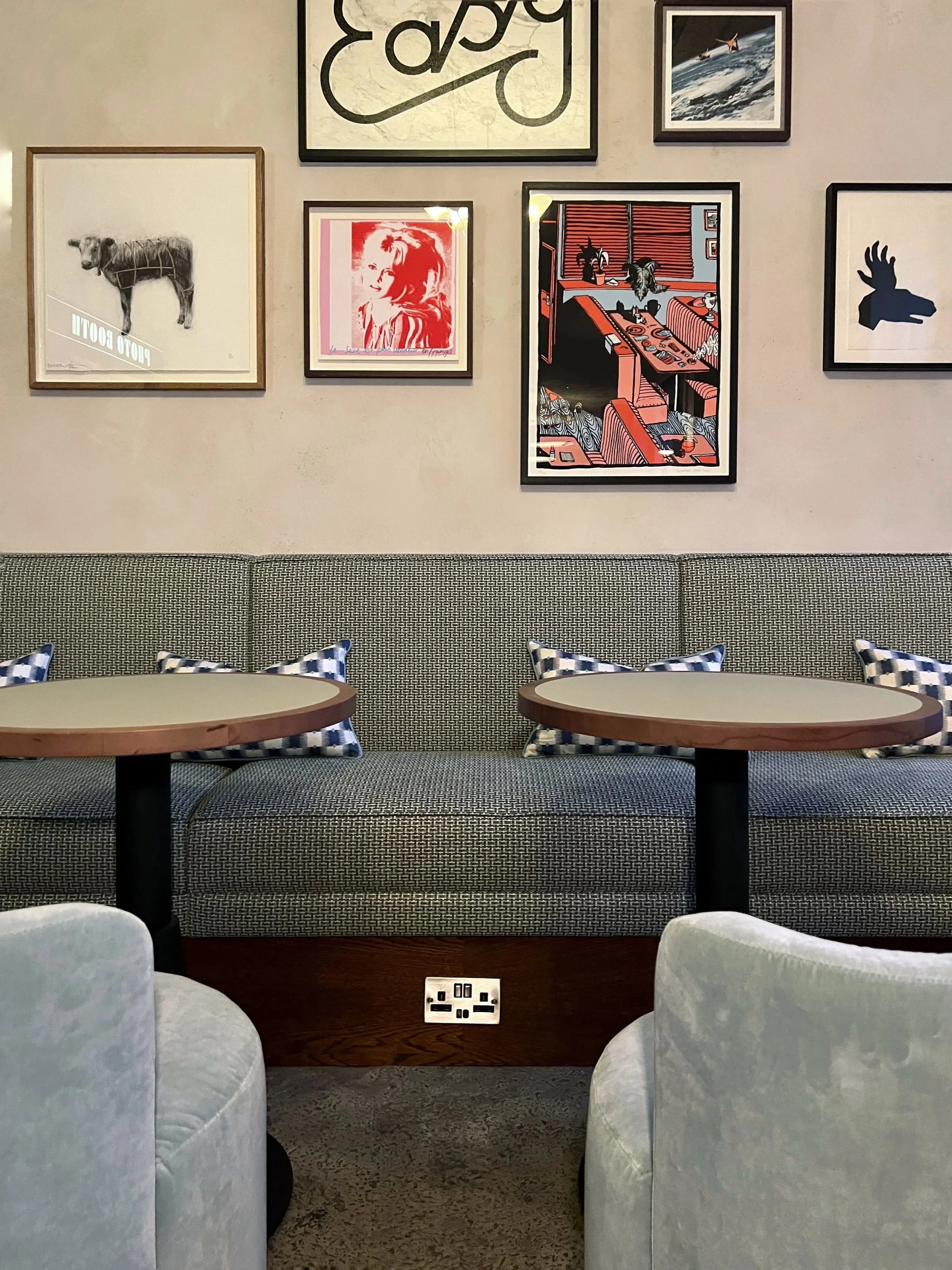 A cozy seating area with a long patterned sofa, round tables, and patterned pillows, decorated with a gallery wall of various framed artworks and pictures.