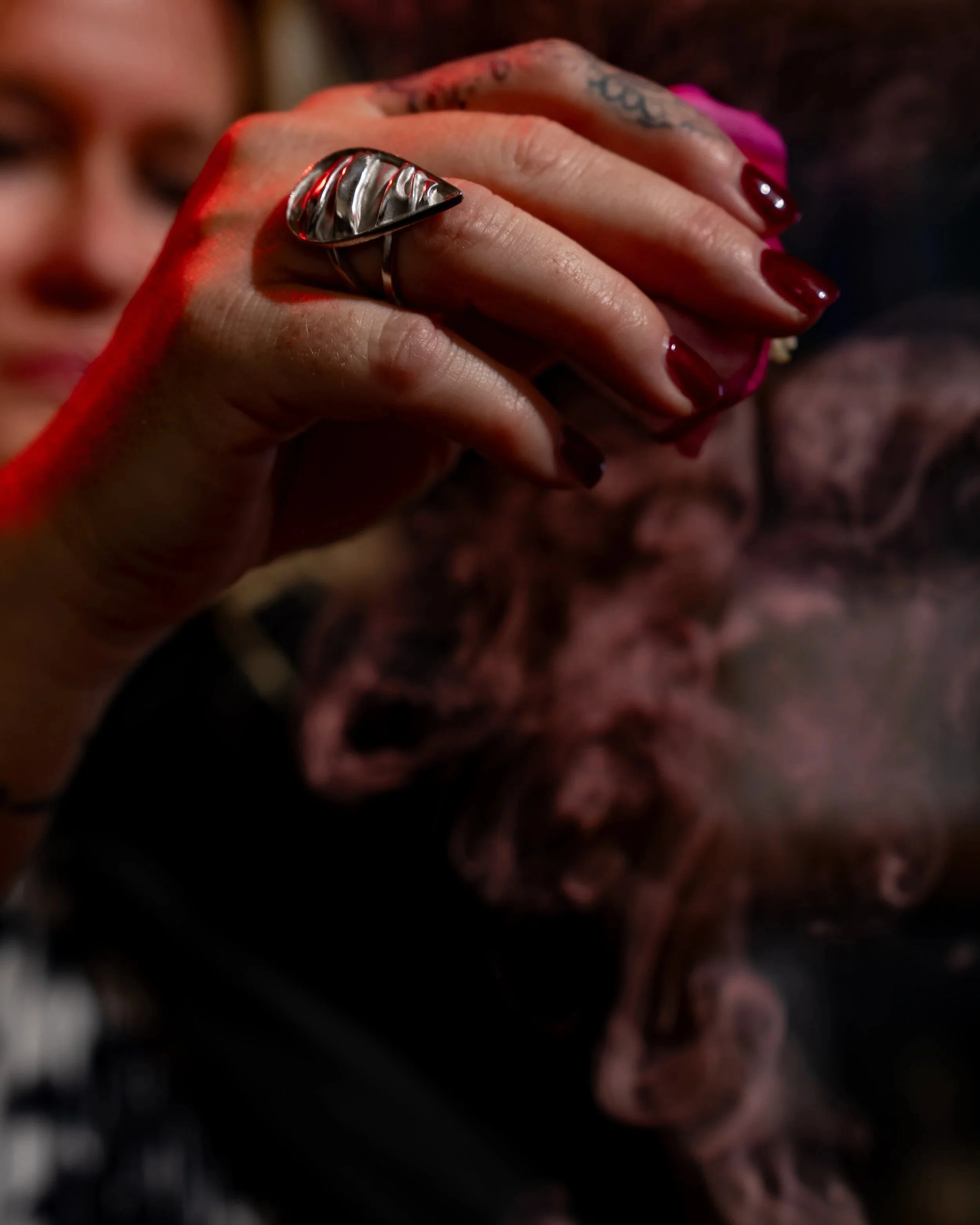 Close-up of a person's hand with painted nails and multiple rings, holding a cigarette with smoke rising.