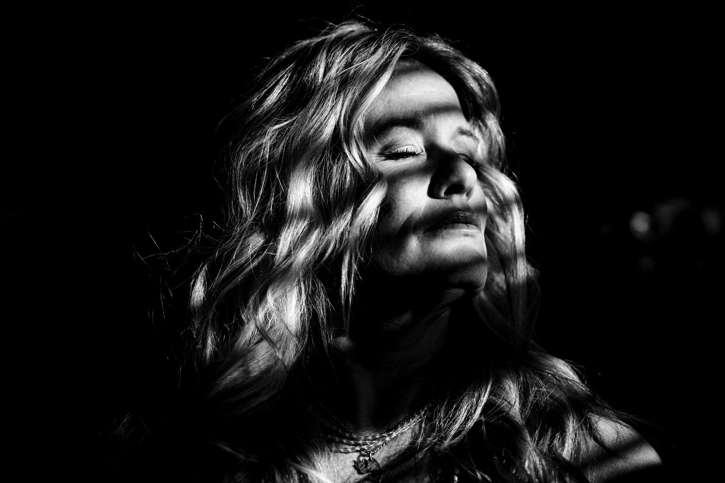 Black and white portrait of a woman with long, wavy hair, closed eyes, and a peaceful expression.