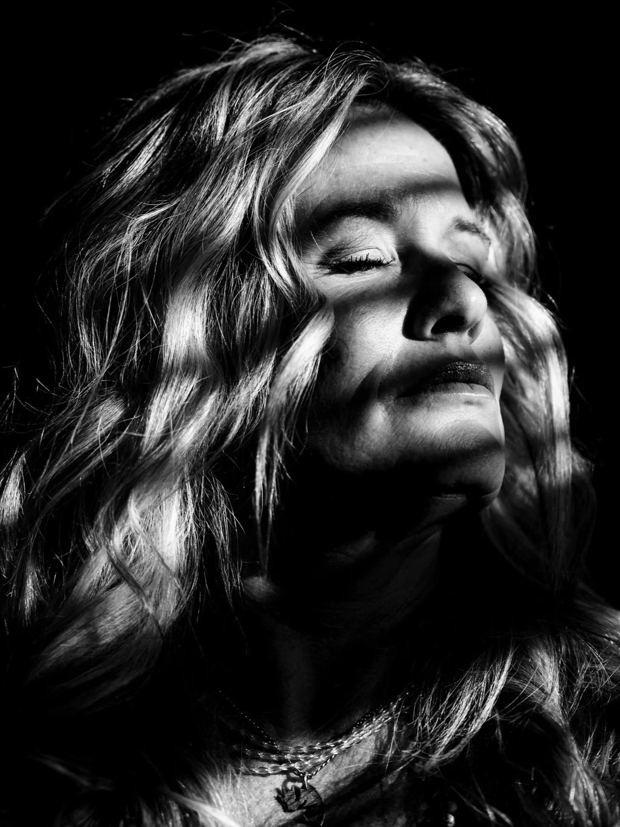 Black and white portrait of a woman with wavy hair and closed eyes, smiling gently, with a shadow cast across her face.