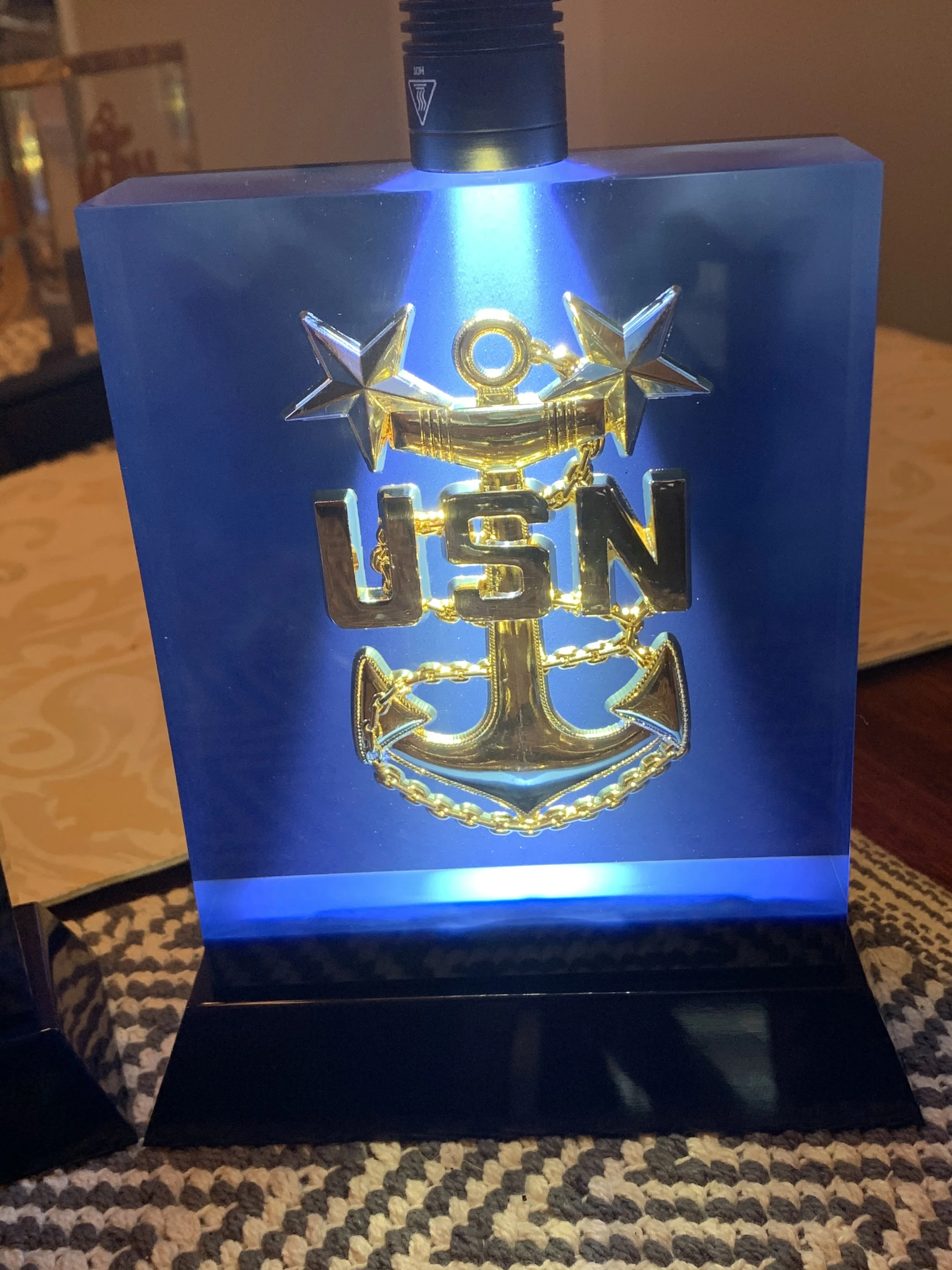 Illuminated decorative plaque with the USN emblem featuring a golden anchor, stars, and chain on a blue background.