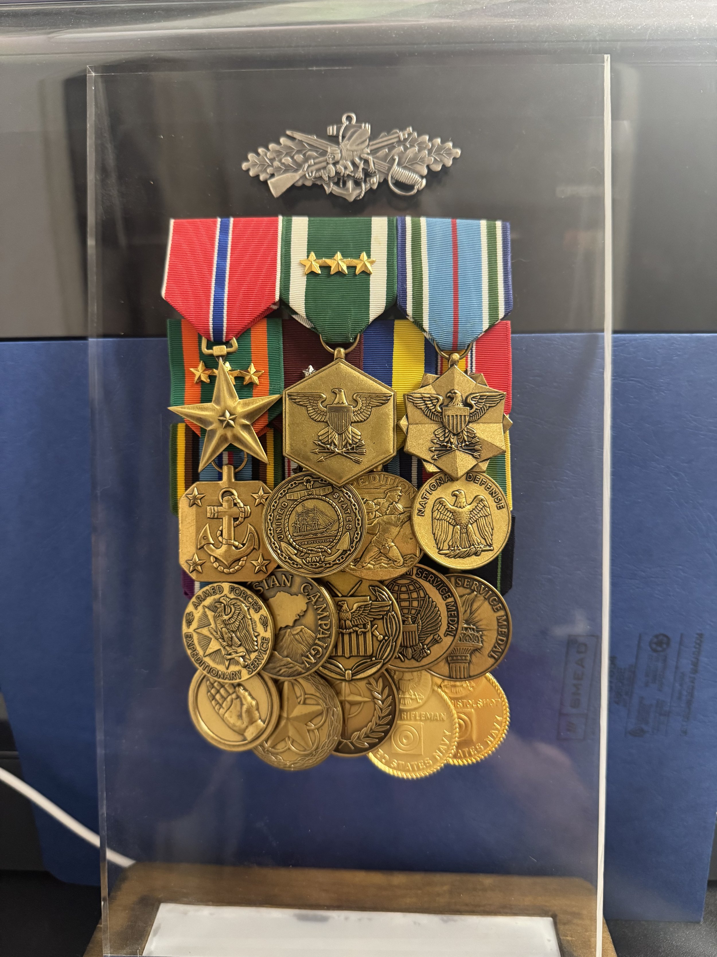 ExhibiGlass Collection of military medals and ribbons displayed in a clear case. The medals awards and insignia badges earned and encased in a protective display
