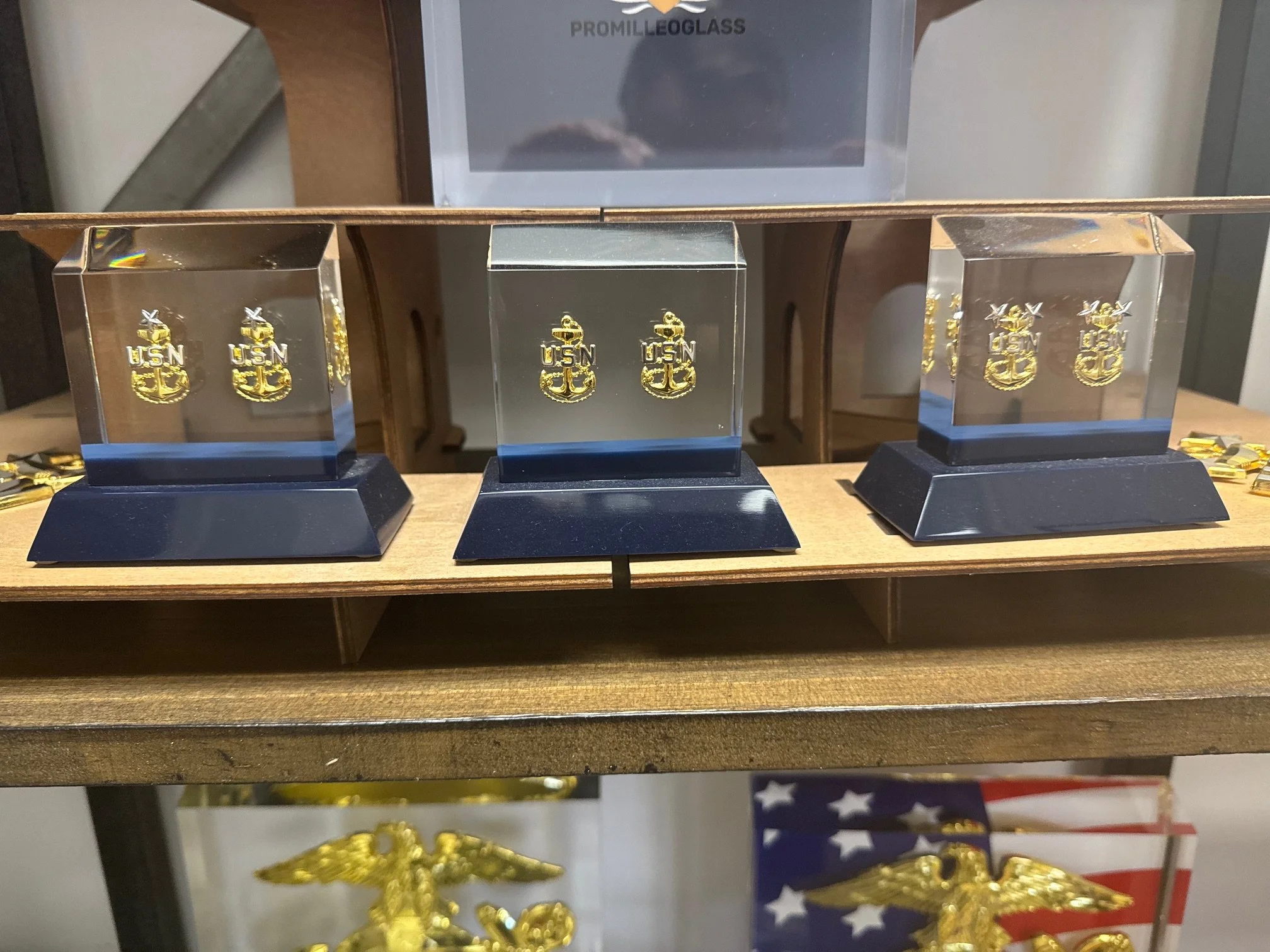 Three glass cubes on a wooden shelf, each bearing a gold U.S. Navy insignia with an anchor, eagle, and shield.