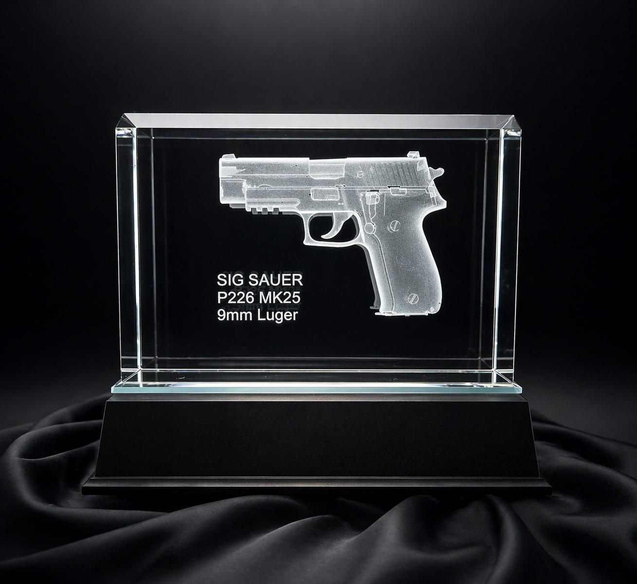 A glass display case showcasing an engraved image of a SIG Sauer P226 MK25 9mm Luger pistol, placed on a black base with a black fabric background.