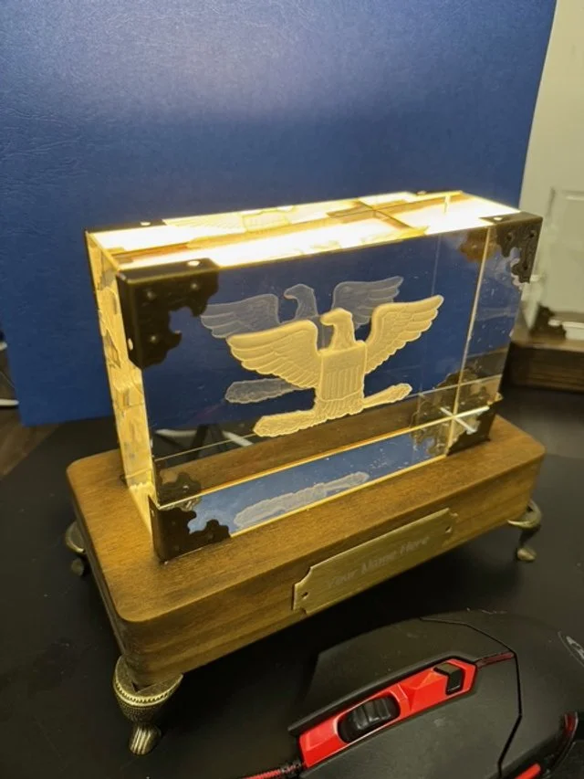 A glass display case with a golden eagle emblem on the front, placed on a wooden base with metal feet.