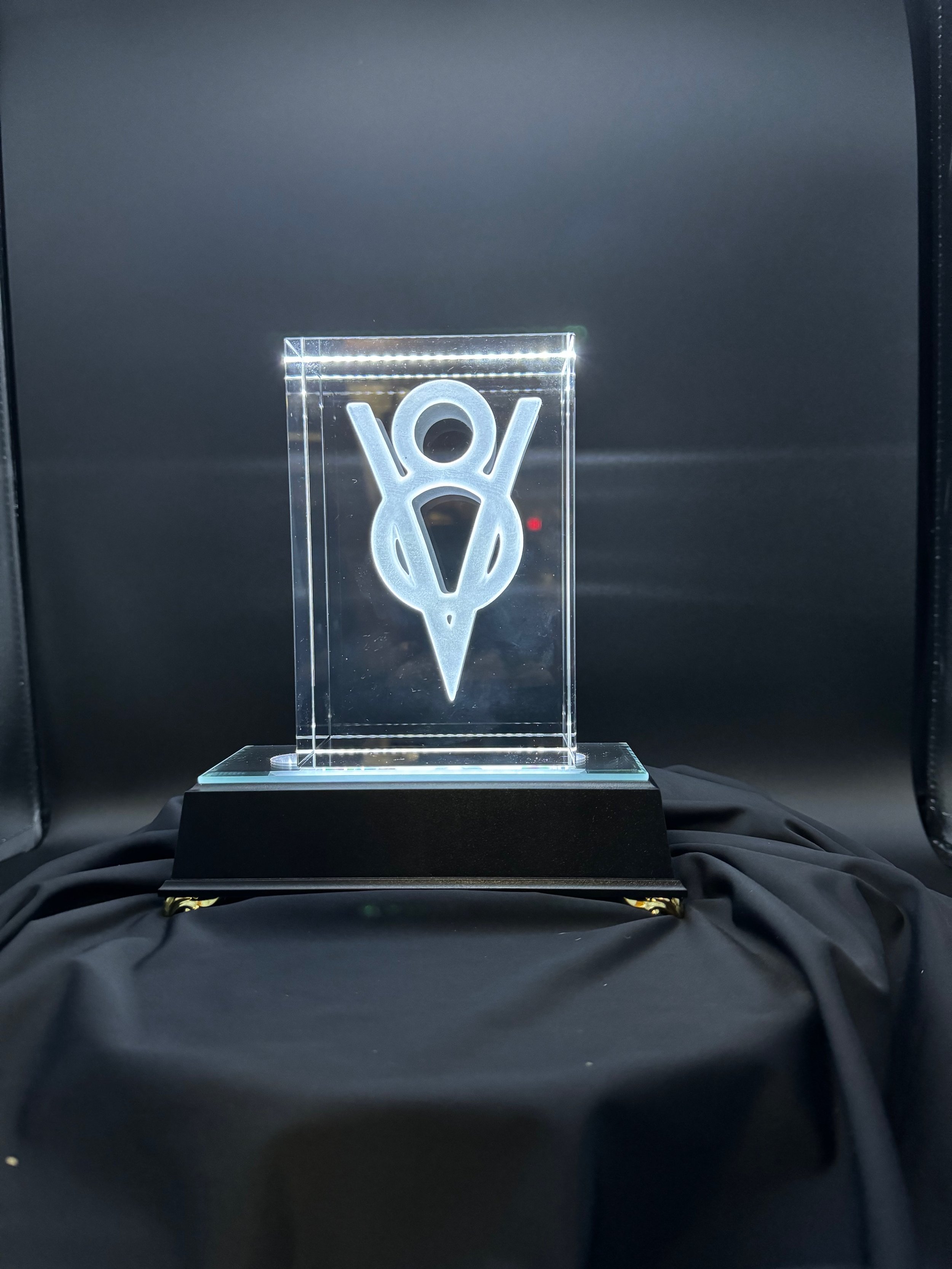 Clear acrylic award with a laser-etched abstract figure, mounted on a black base, displayed on black fabric against a dark background.