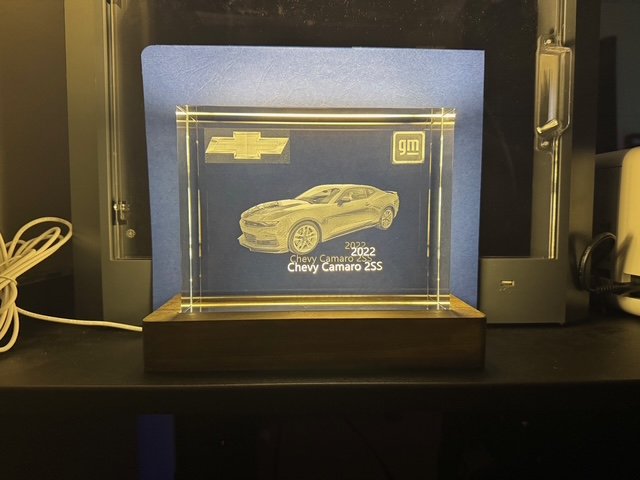 A clear acrylic plaque featuring an engraved image of a 2022 Chevy Camaro 2SS, Chevy logo, GM logo, and model details, displayed on a wooden base.