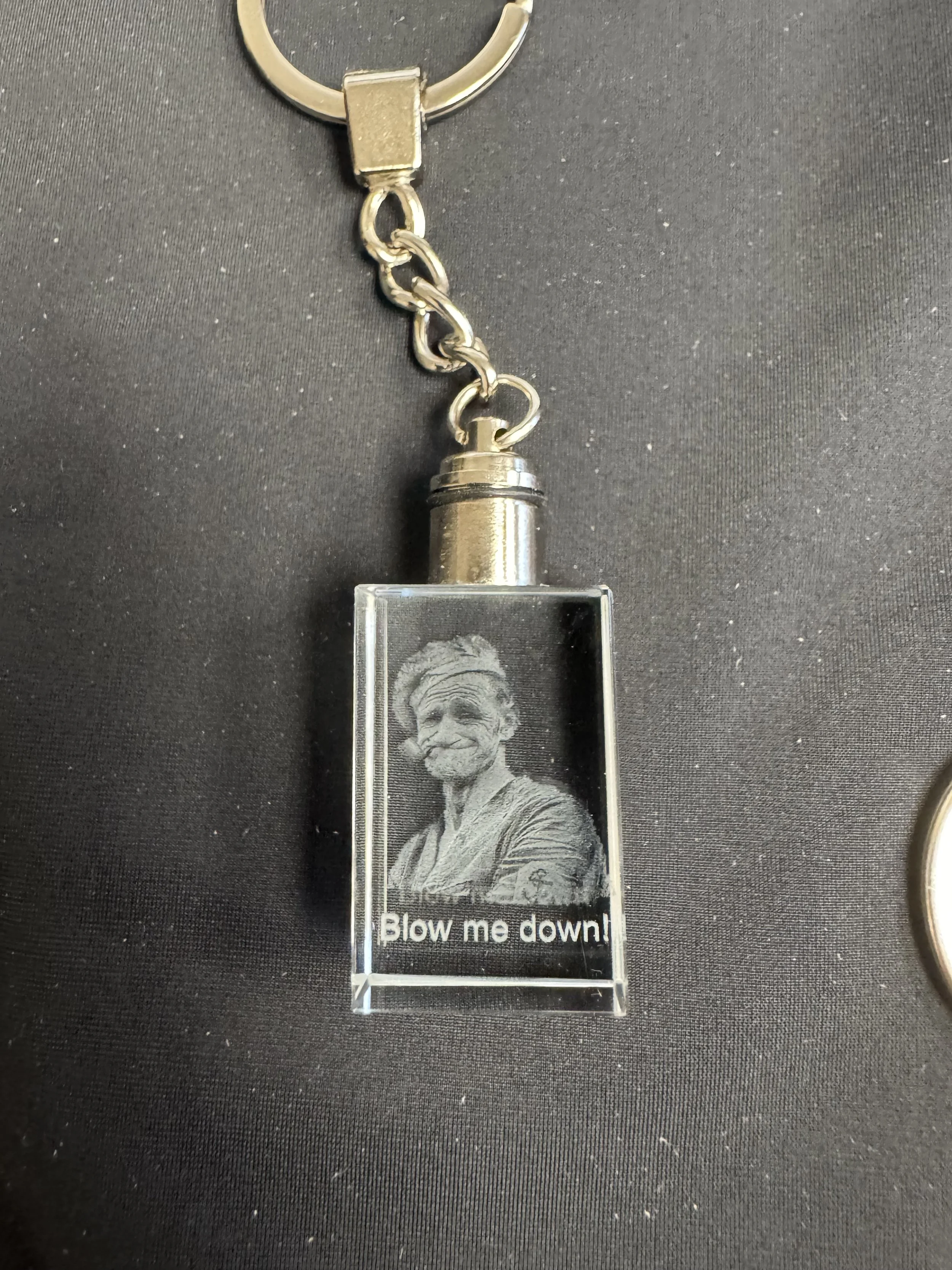 A keychain with a glass pendant featuring a black and white image of a man with a bandana, and the text 'Blow me down!' underneath.