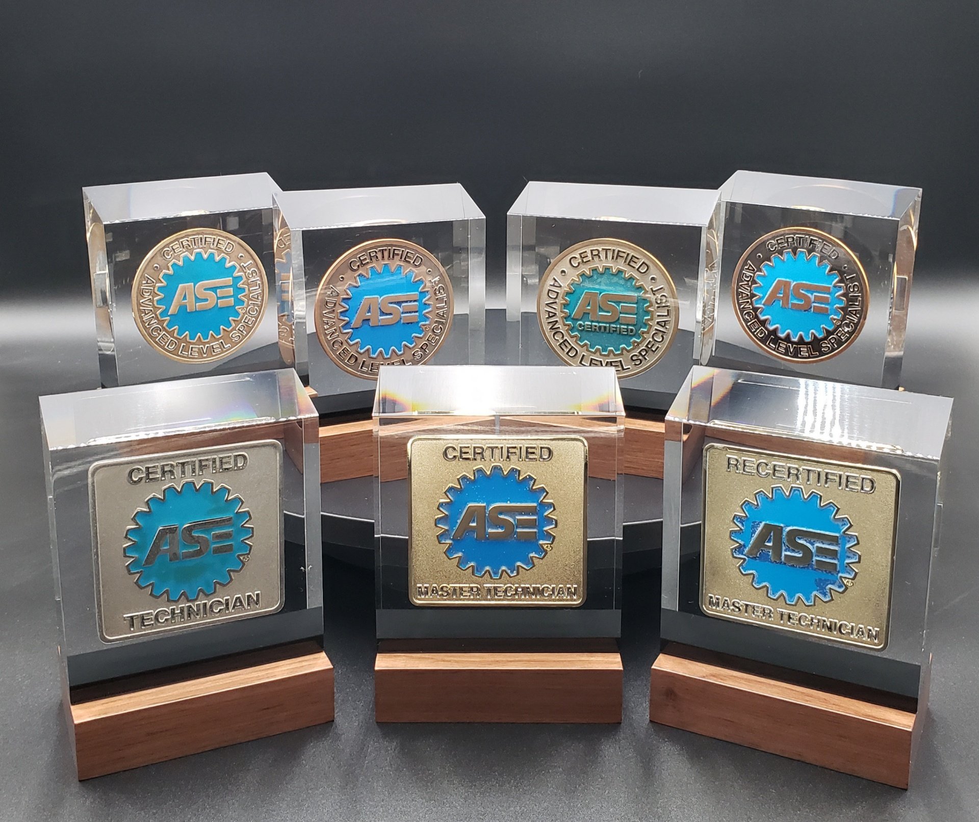 Collection of ASE badges on wooden and acrylic bases, including certified, master technician, and specialized technician awards.