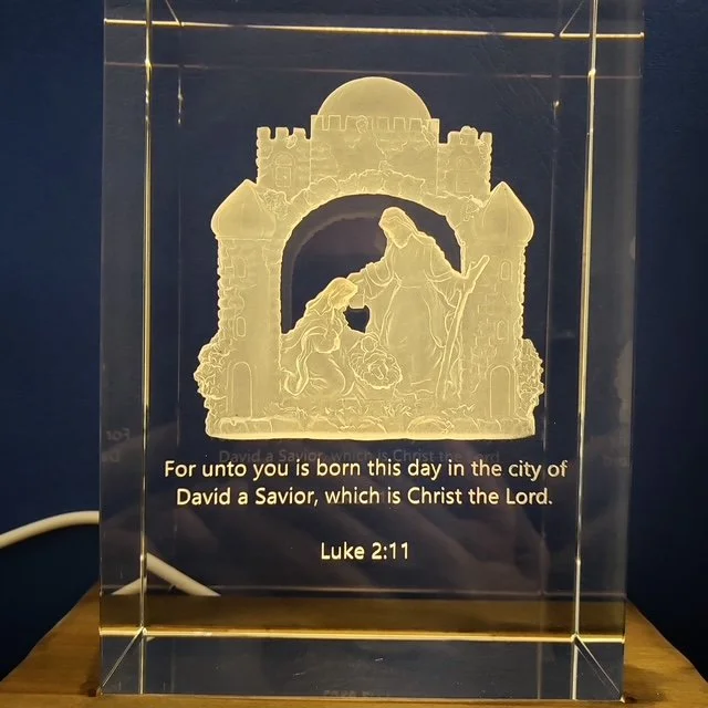 A clear glass plaque with an engraved scene of Mary and Baby Jesus in a manger, with a castle and archway in the background. The plaque has a Bible verse from Luke 2:11 inscribed at the bottom.