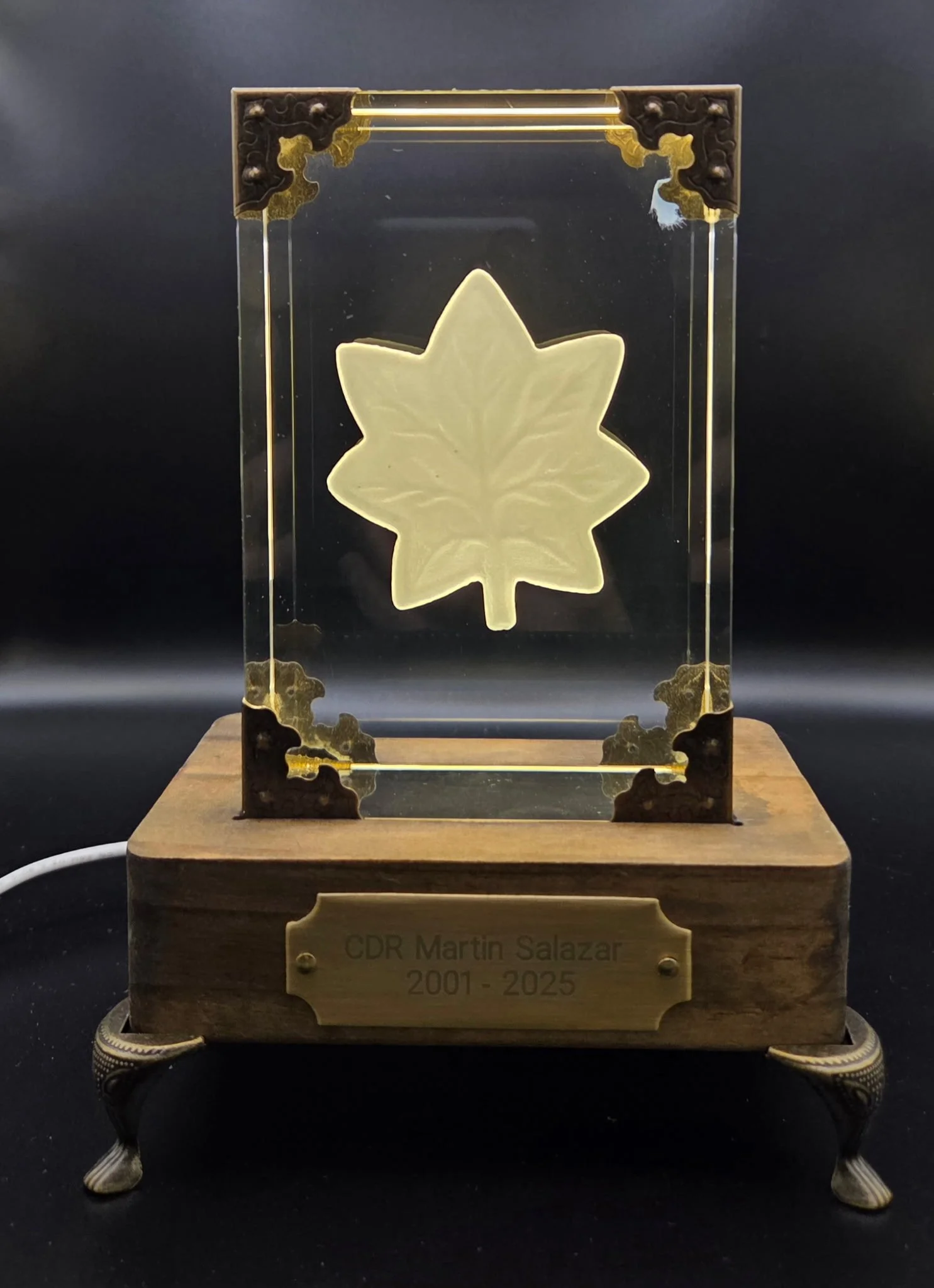 A decorative memorial tribute with a wooden base and metal plaque, featuring a glass panel with a carved maple leaf, dedicated to CDR Martin Salazar, who lived from 2001 to 2025.