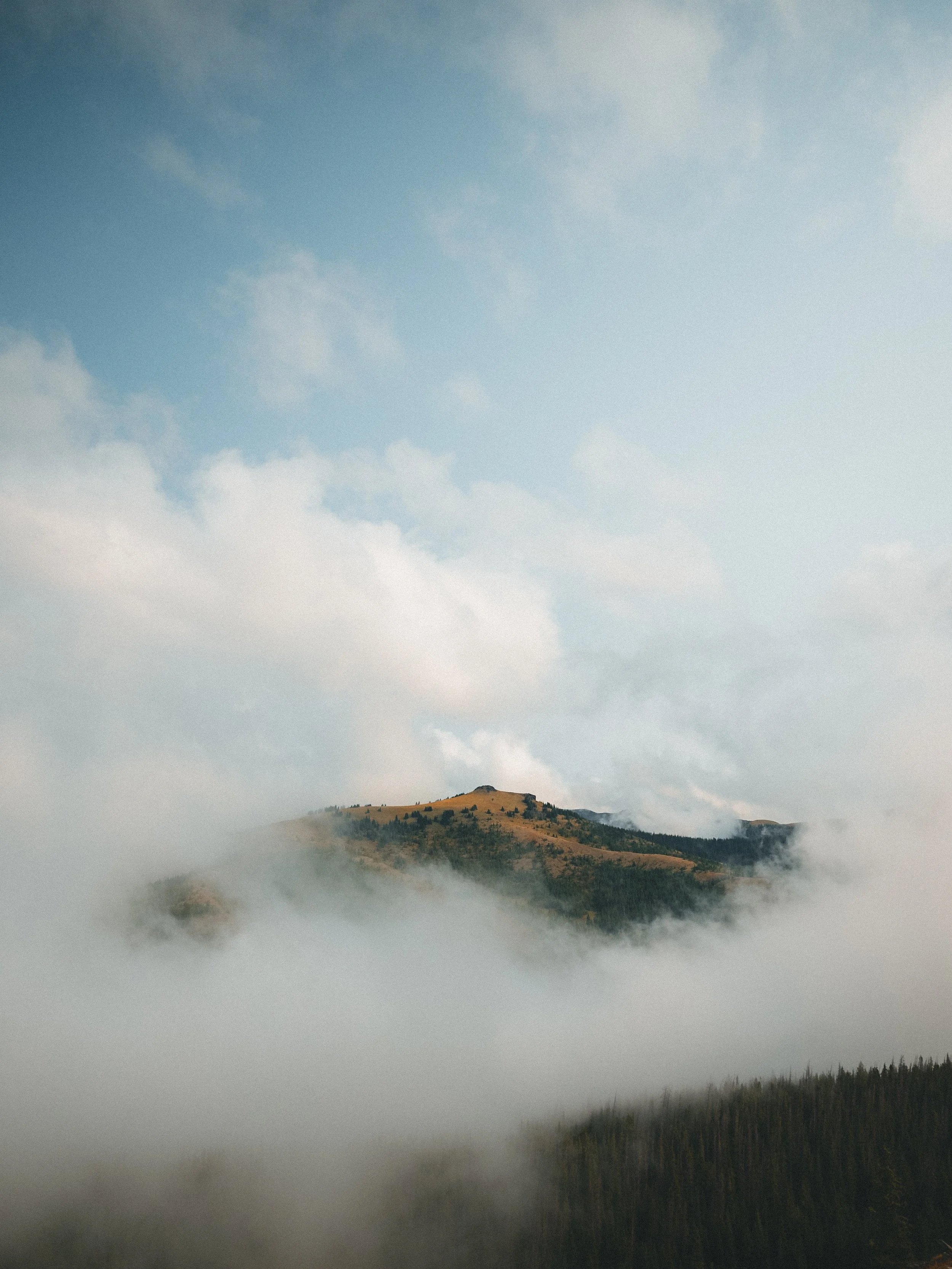 Mountain landscape with clouds and mist in the foreground and blue sky with clouds above.