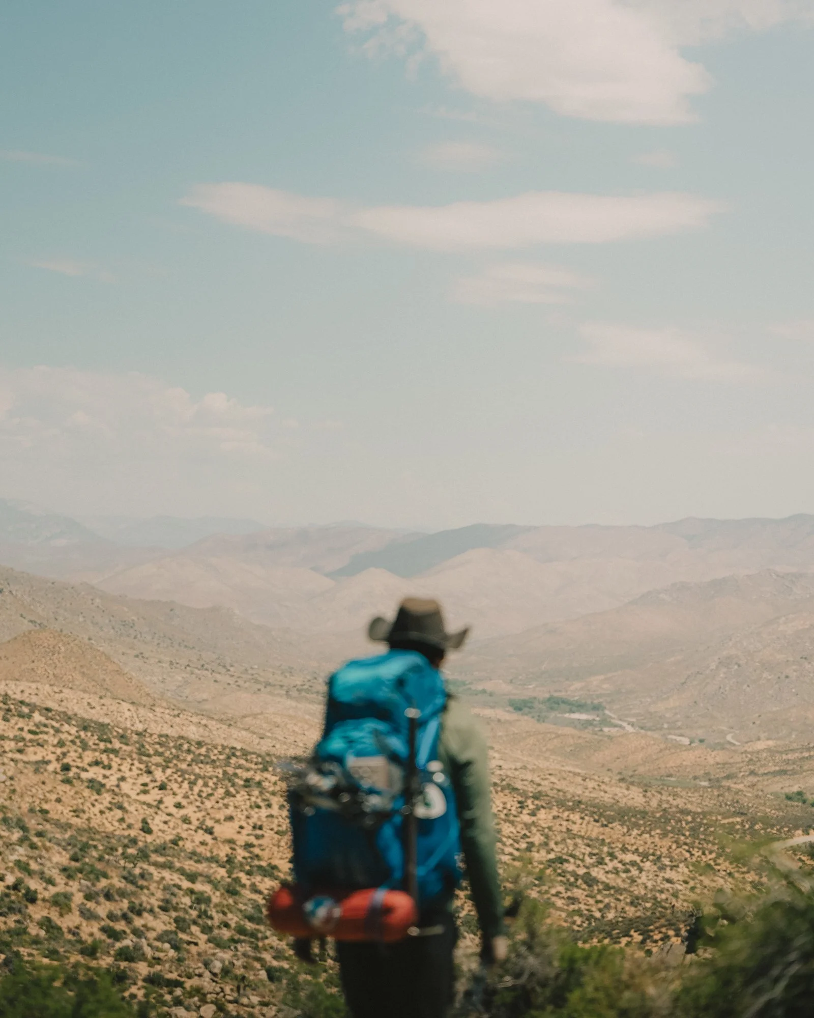 A person with a backpack hiking in a desert landscape with mountains and blue sky.