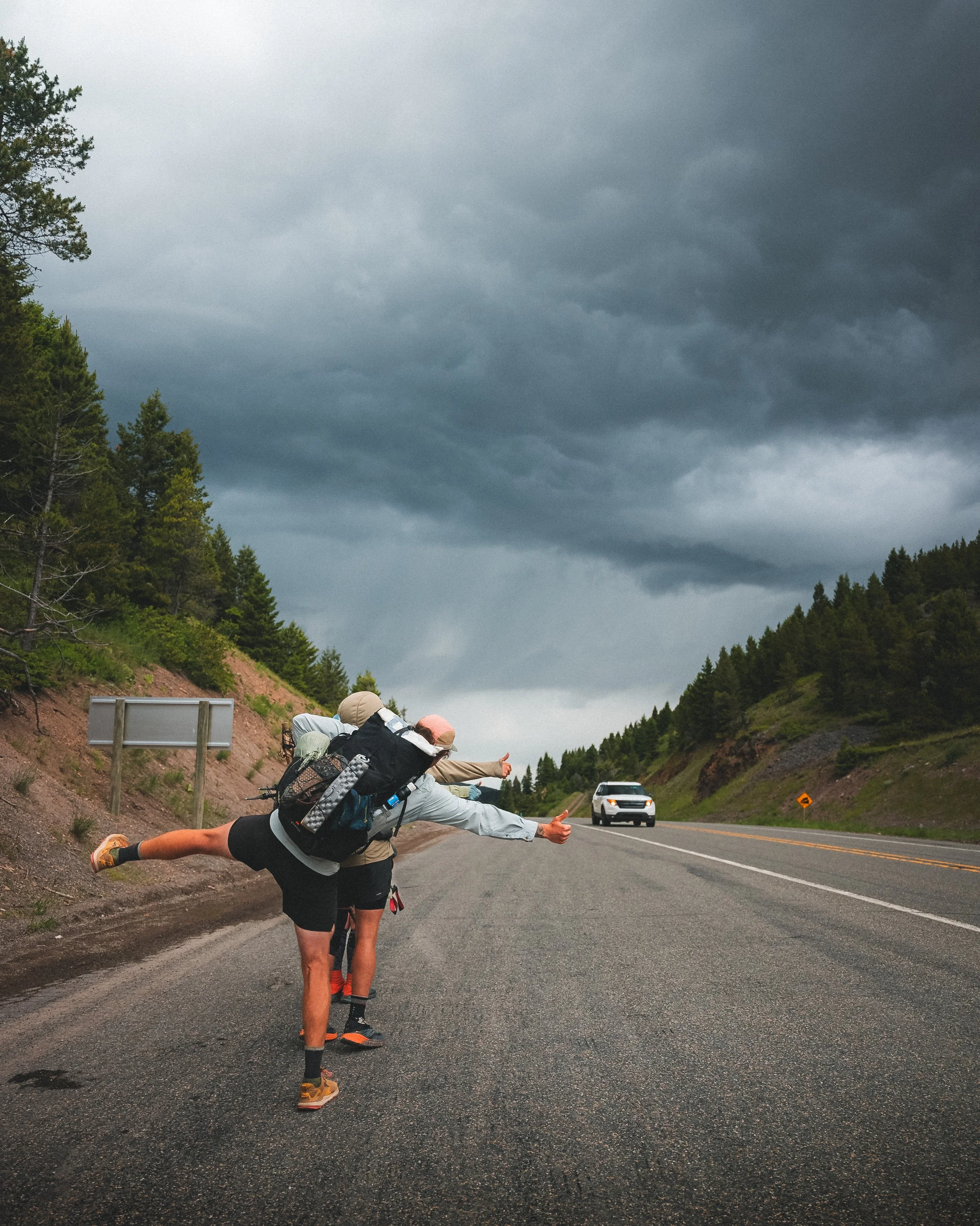 Group of hikers hitchhiking on a mountain road with dark stormy clouds overhead