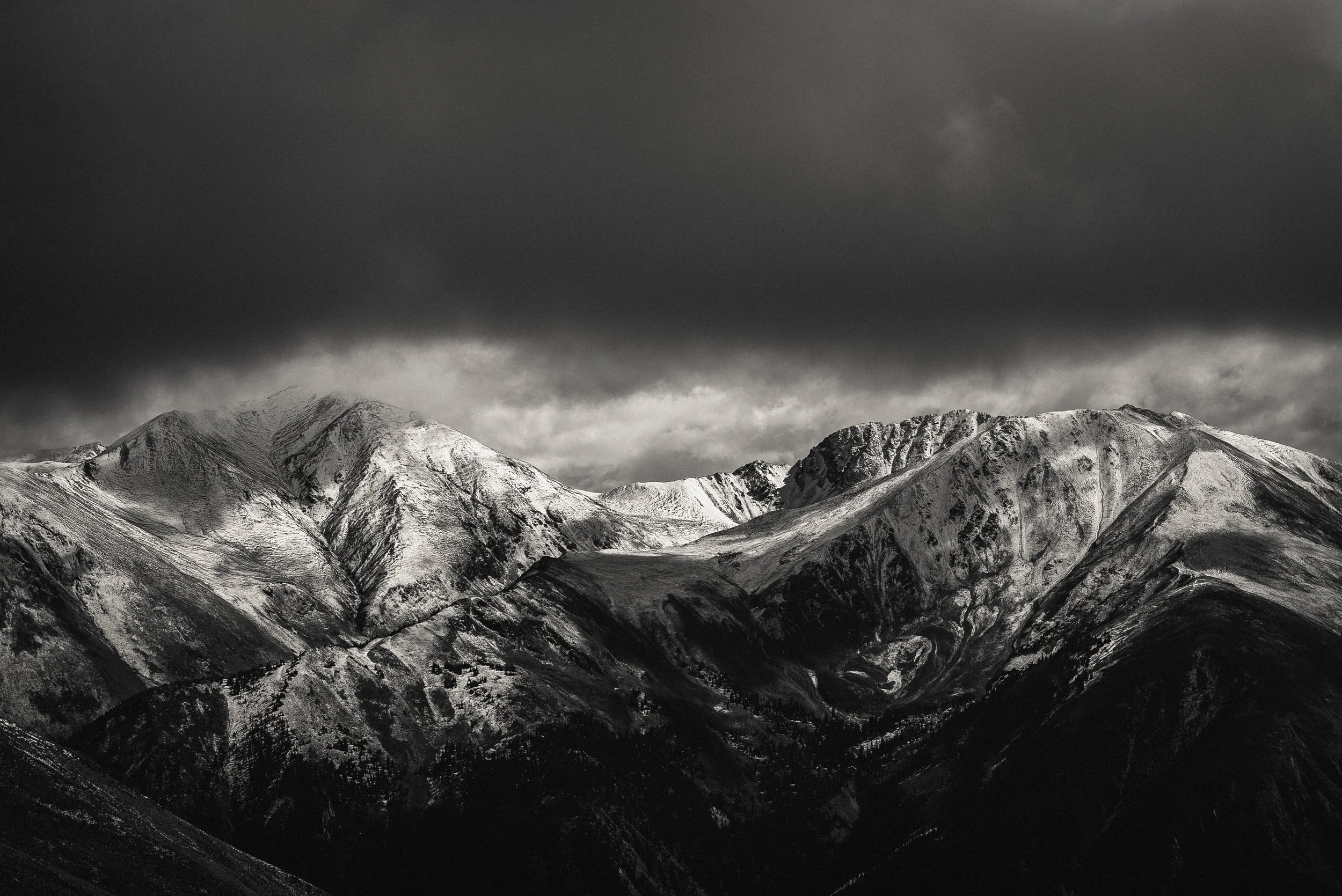 Snow-covered mountain range under dark, cloudy sky.