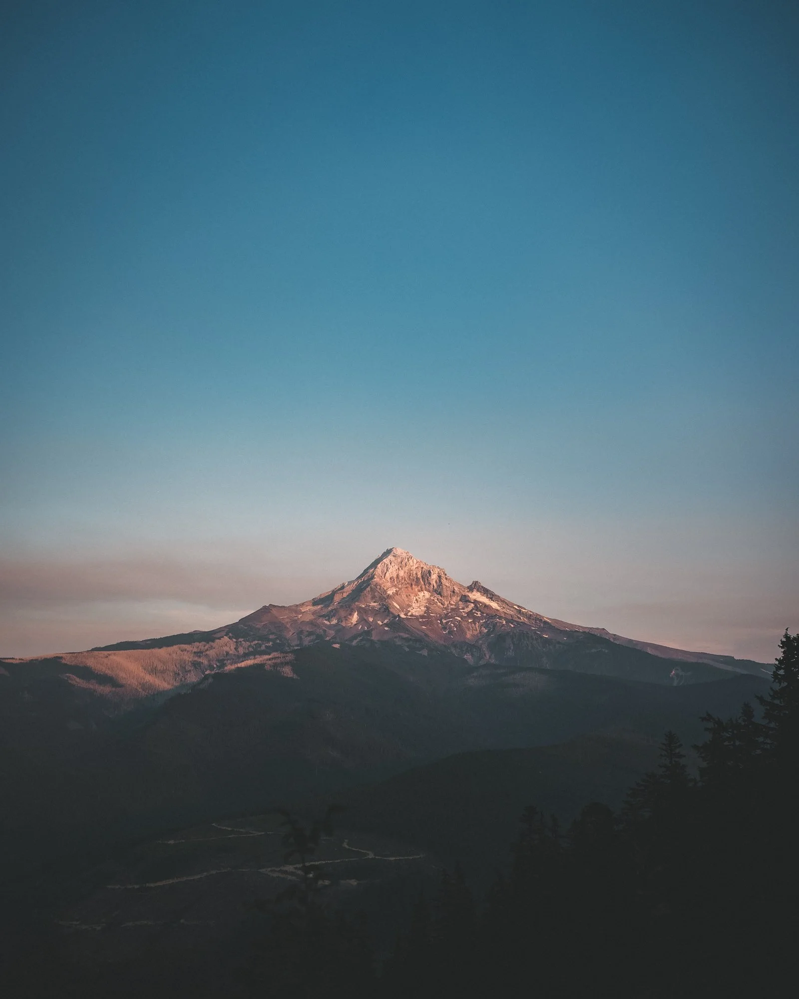 A mountain with a snow-capped peak against a clear blue sky during sunset or sunrise.