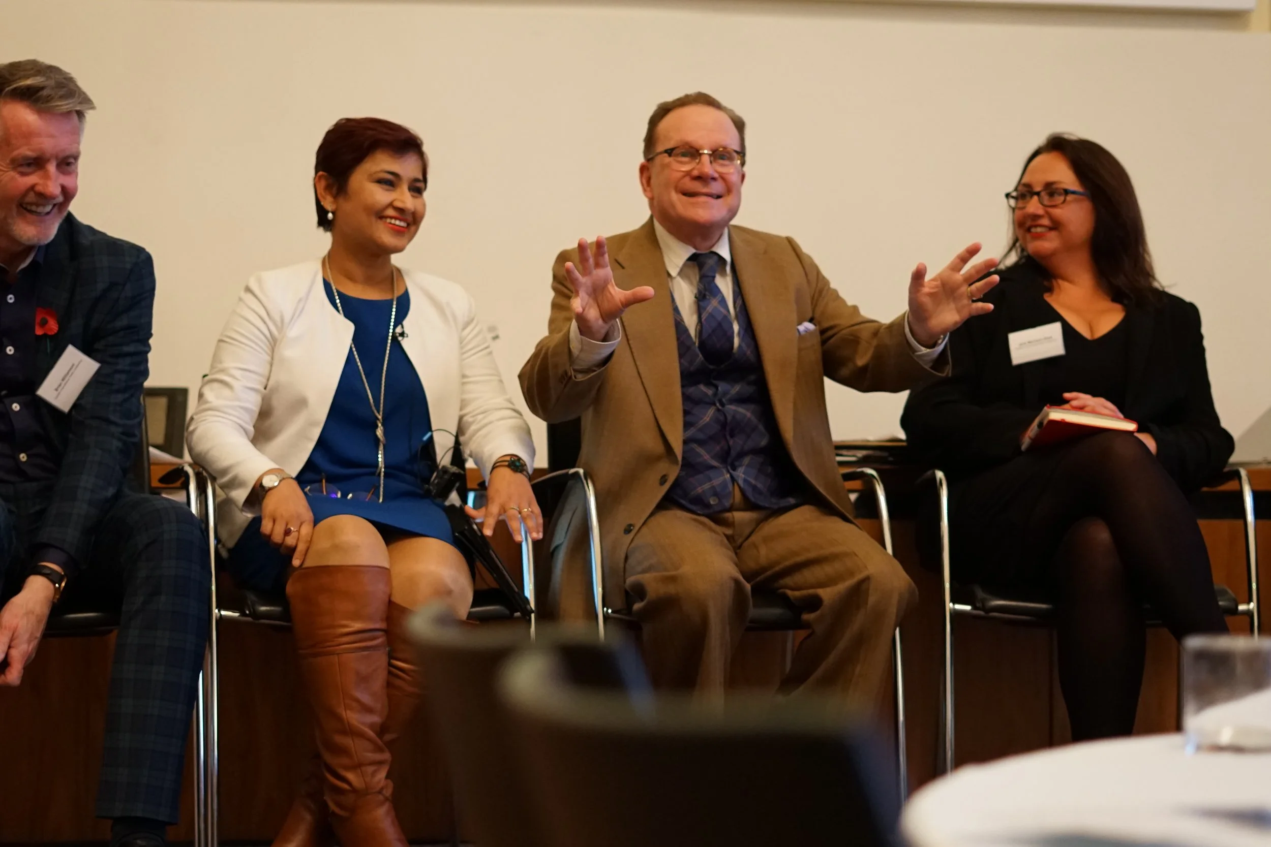 Four people sitting on chairs in a panel discussion or meeting, smiling and engaging with each other.