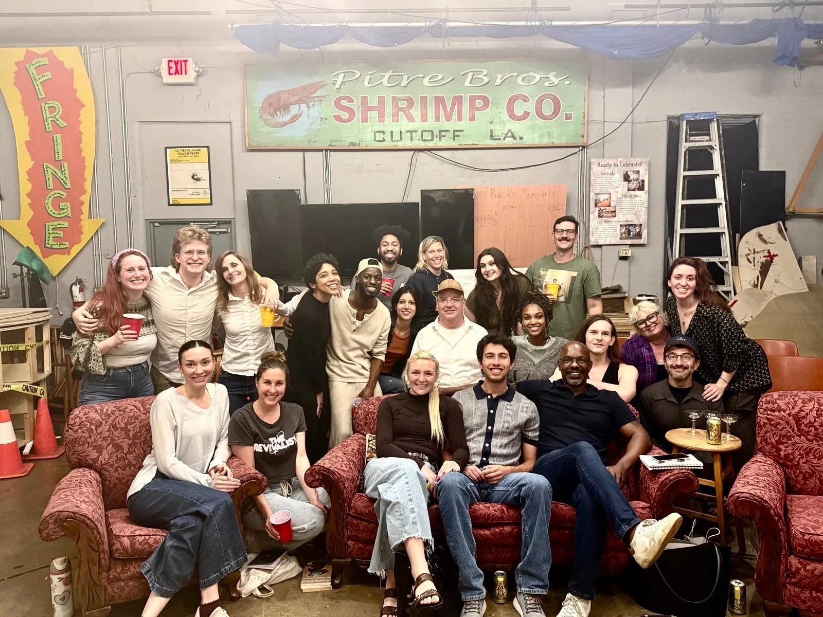 A group of people smiling and posing for a photo in a room with furniture and signs, including a large green and red sign that says "Pitre Bros. Shrimp Co."

