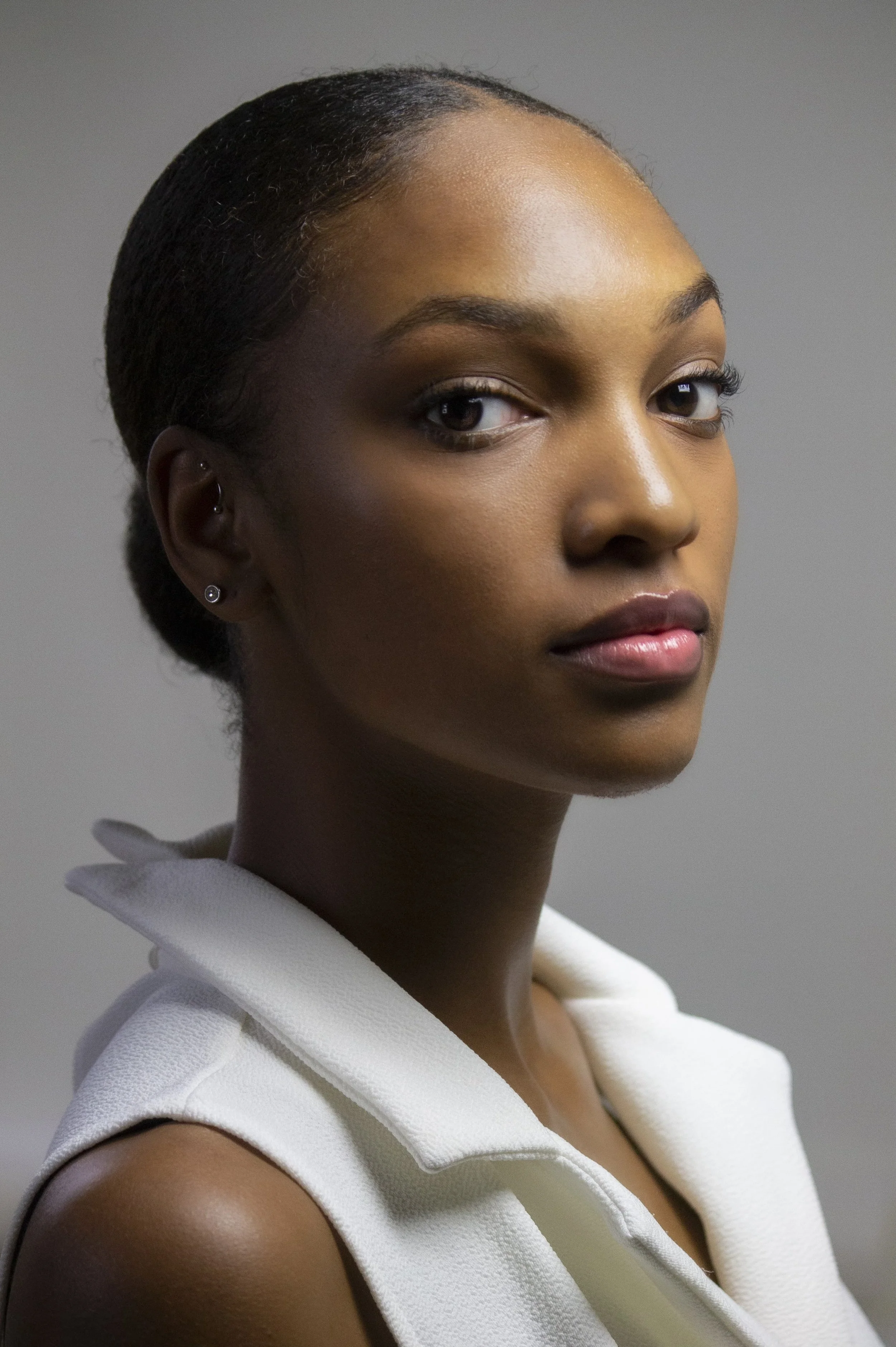 Close-up portrait of a young African American woman with a calm expression, wearing a white sleeveless top, plain gray background